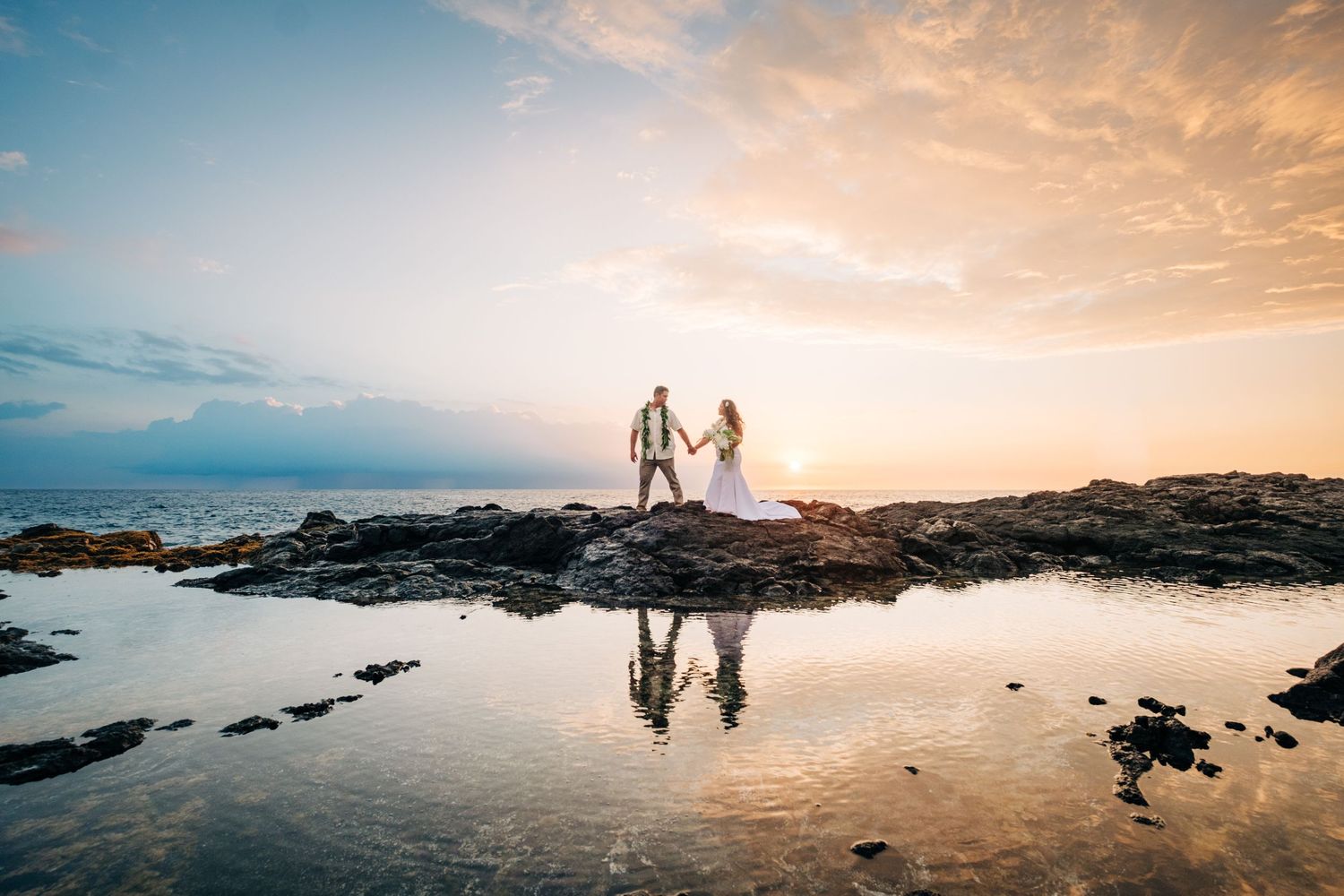 Panoramic sunset beach scene with silhouettes and volcanic rocks along the Hawaiian coastline at Kukio Beach, Kona, Big Island of Hawaii.