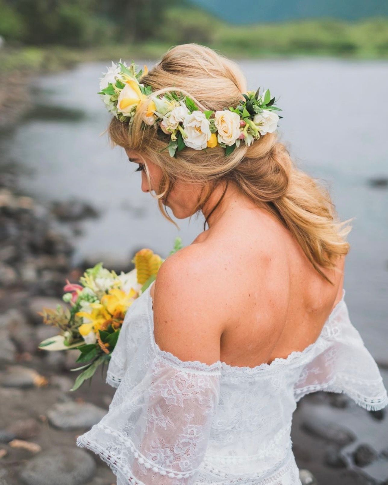Bride in off-shoulder lace dress with floral crown poses by tropical coastline on the Big Island of Hawaii.