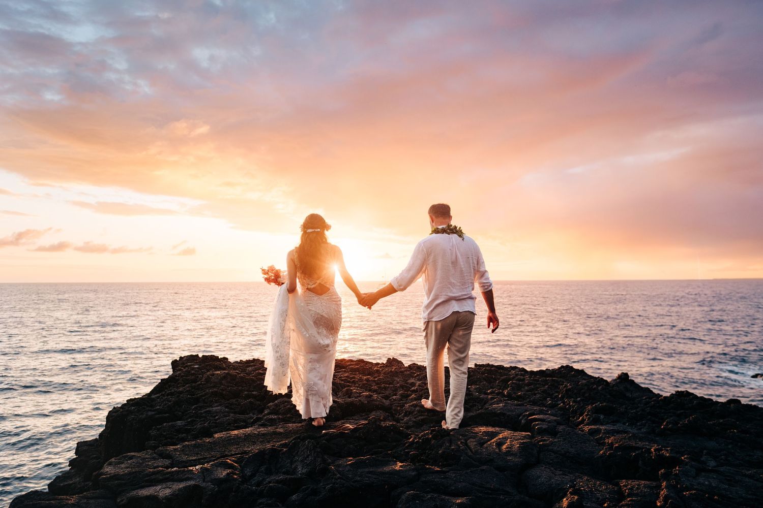 Couple walking along rocky coastline during golden hour sunset at Outrigger Kona Resort, Big Island Hawaii.