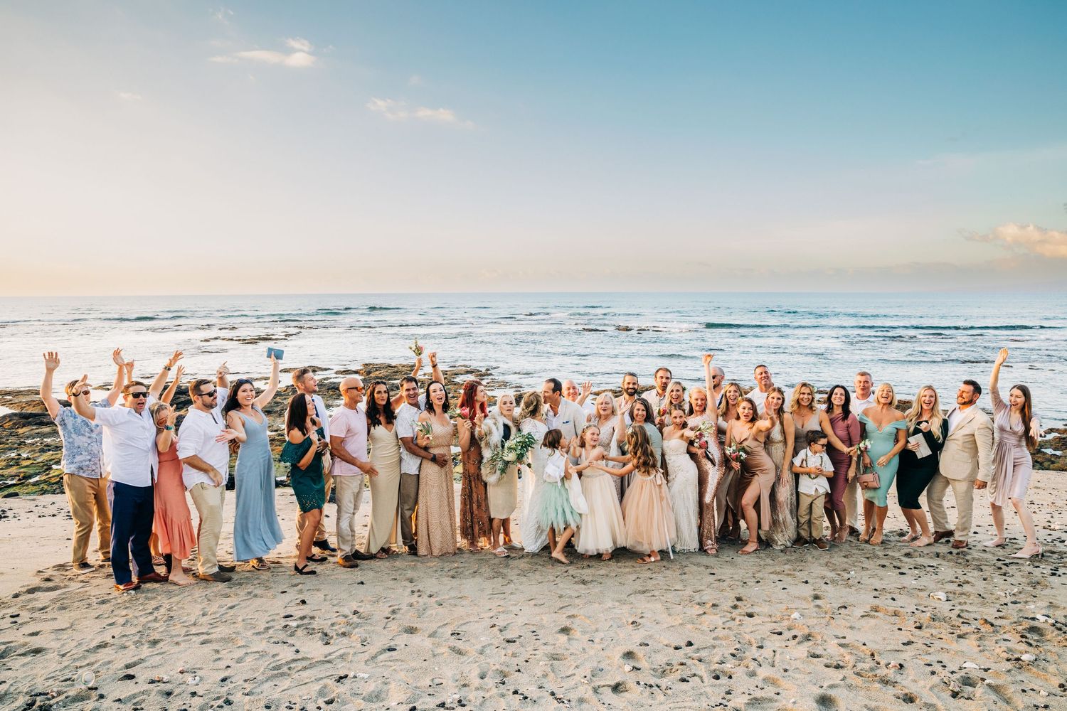 Large group of wedding guests posed together on a tropical beach at sunset at Mauna Lani Beach Resort.