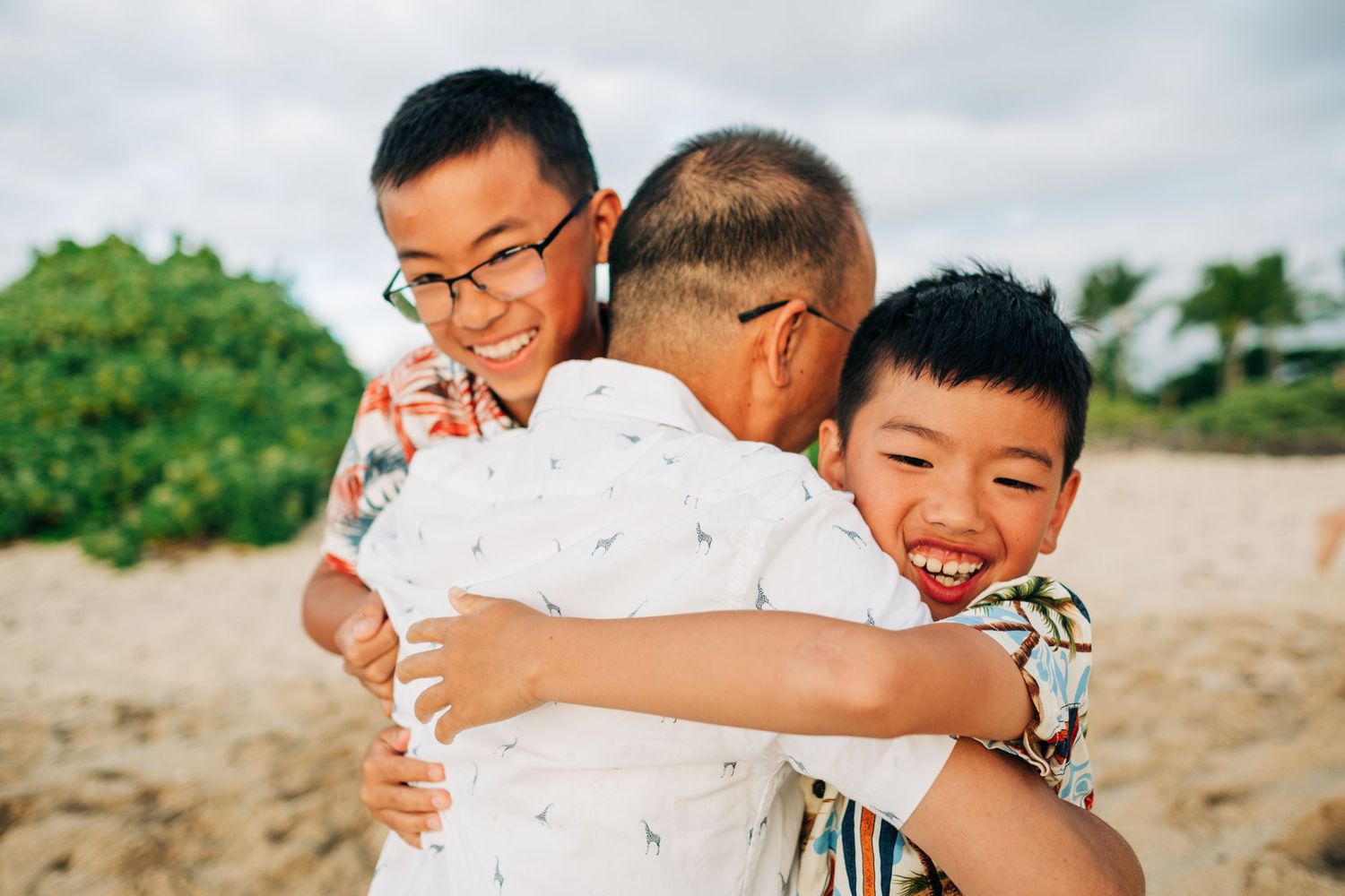 Joyful embraces shared on sunny beach with mountains in background at Kukio Beach, Kona, Big Island Hawaii.