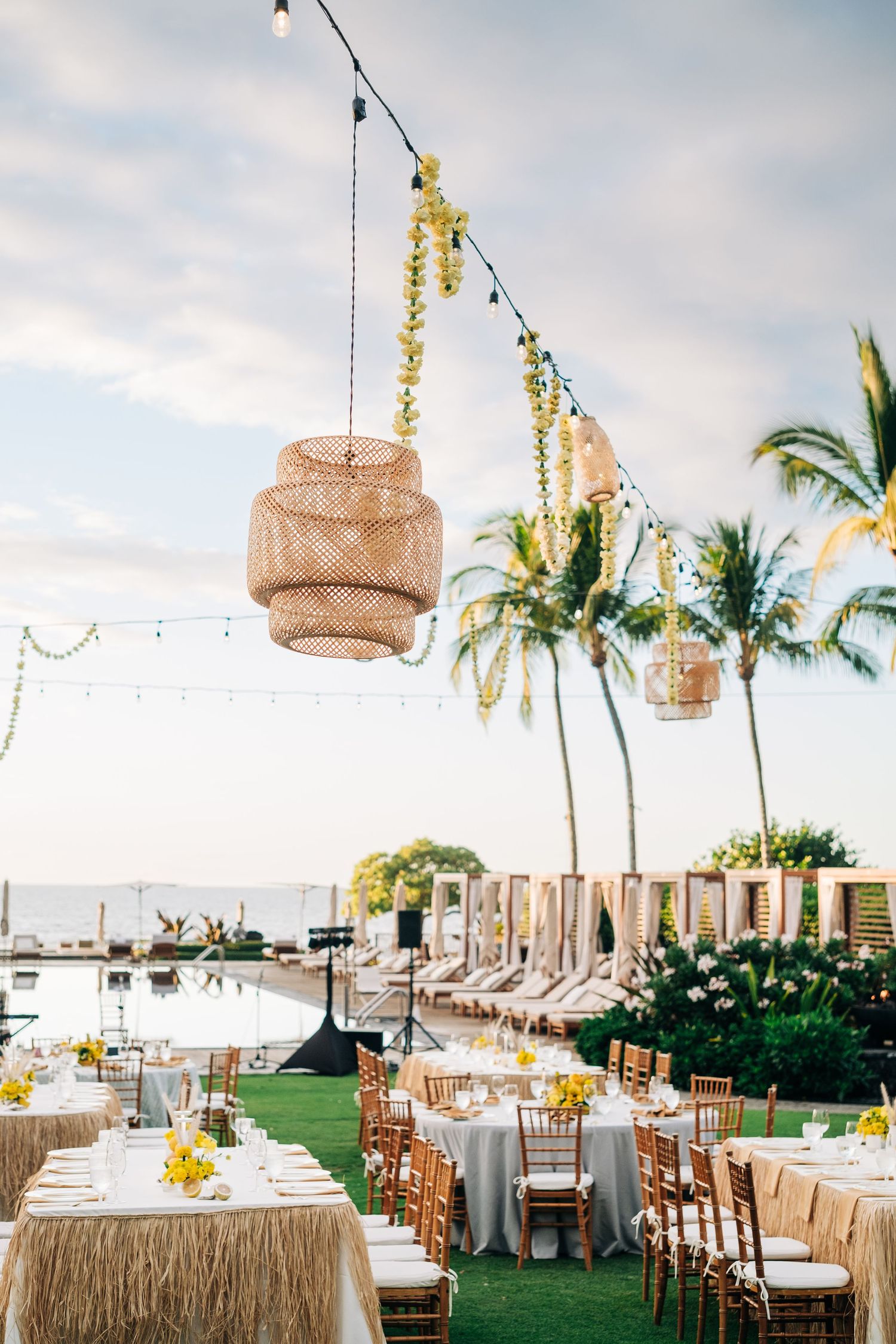 Tropical wedding reception setup with hanging woven lanterns and string lights over dining tables at a Four Seasons Hualalai Event.
