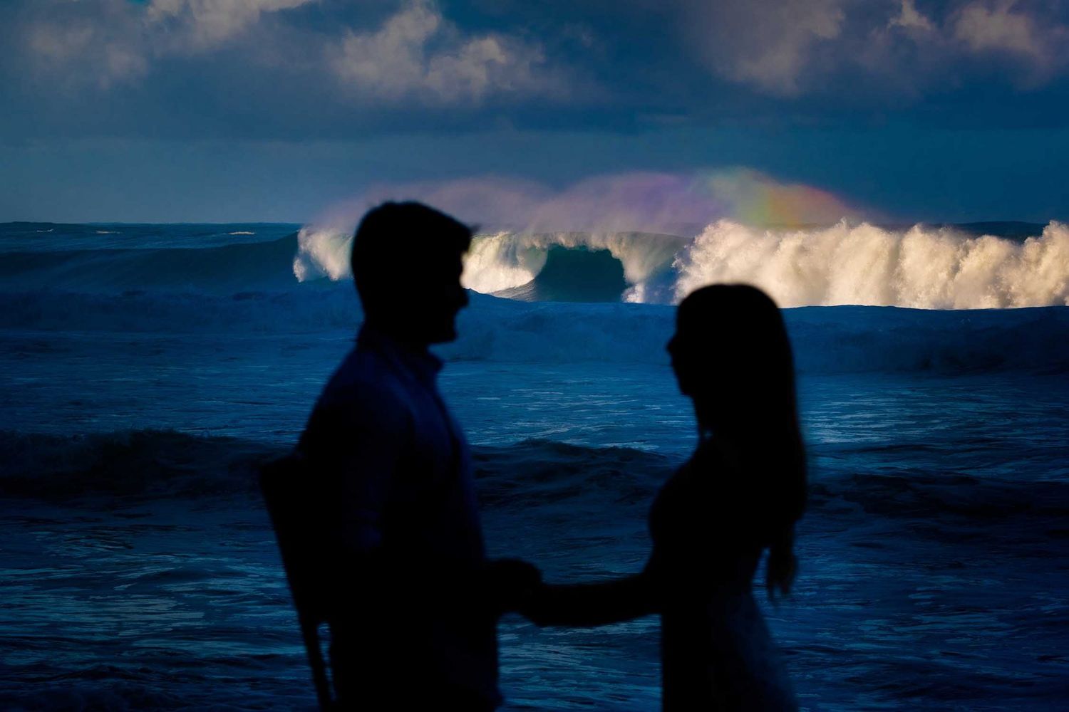 Silhouettes against a dramatic ocean sunset with crashing waves on the Big Island of Hawaii.