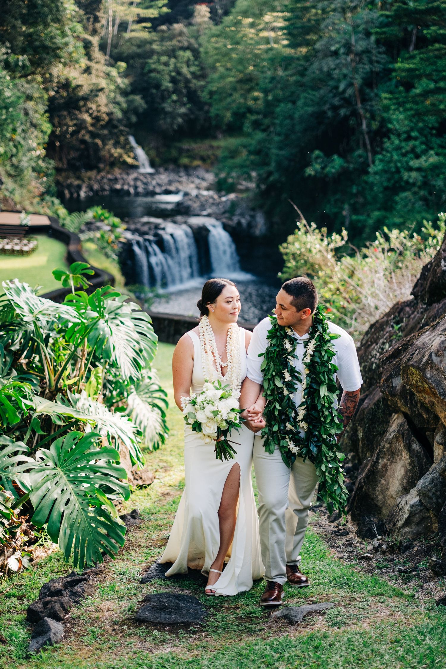 Newlyweds share an intimate moment by a waterfall surrounded by tropical greenery at the Falls at Reeds Island, Hilo, Big Island of Hawaii.