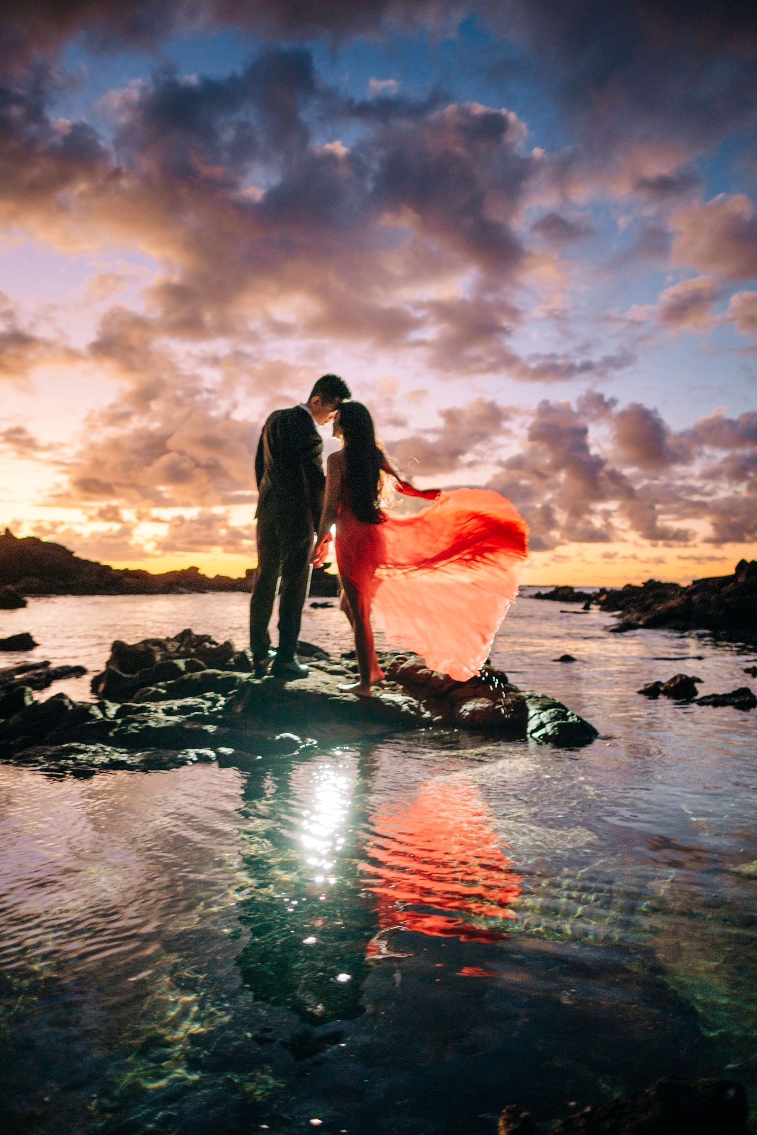 Sunset beach photography session with flowing red fabric creating dramatic silhouettes.on wet sand at Kikaua Point Beach, Kona.