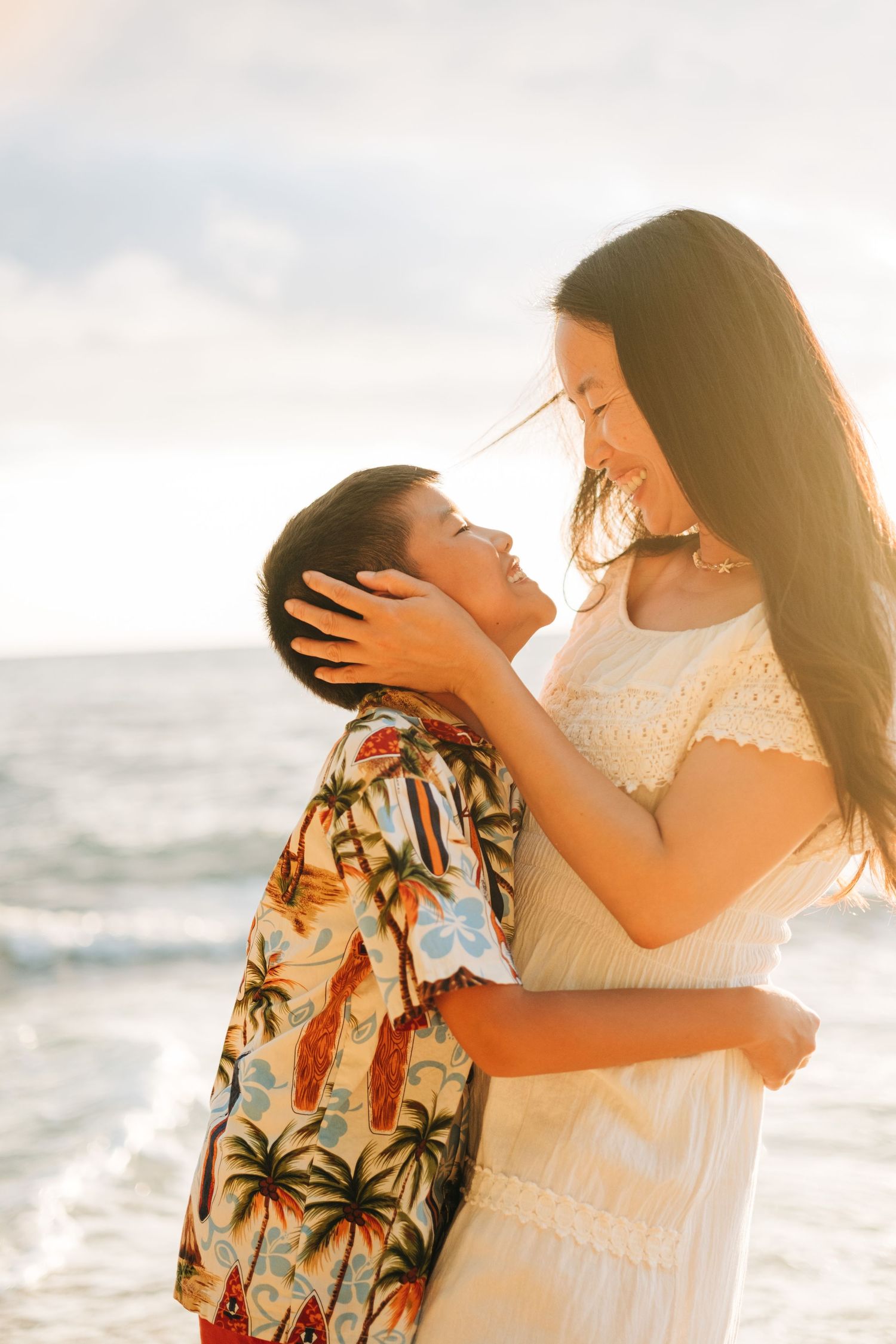 Couple embracing in warm sunlight on a beach with palm trees in background. Kona Family Photography, Big Island of Hawaii.