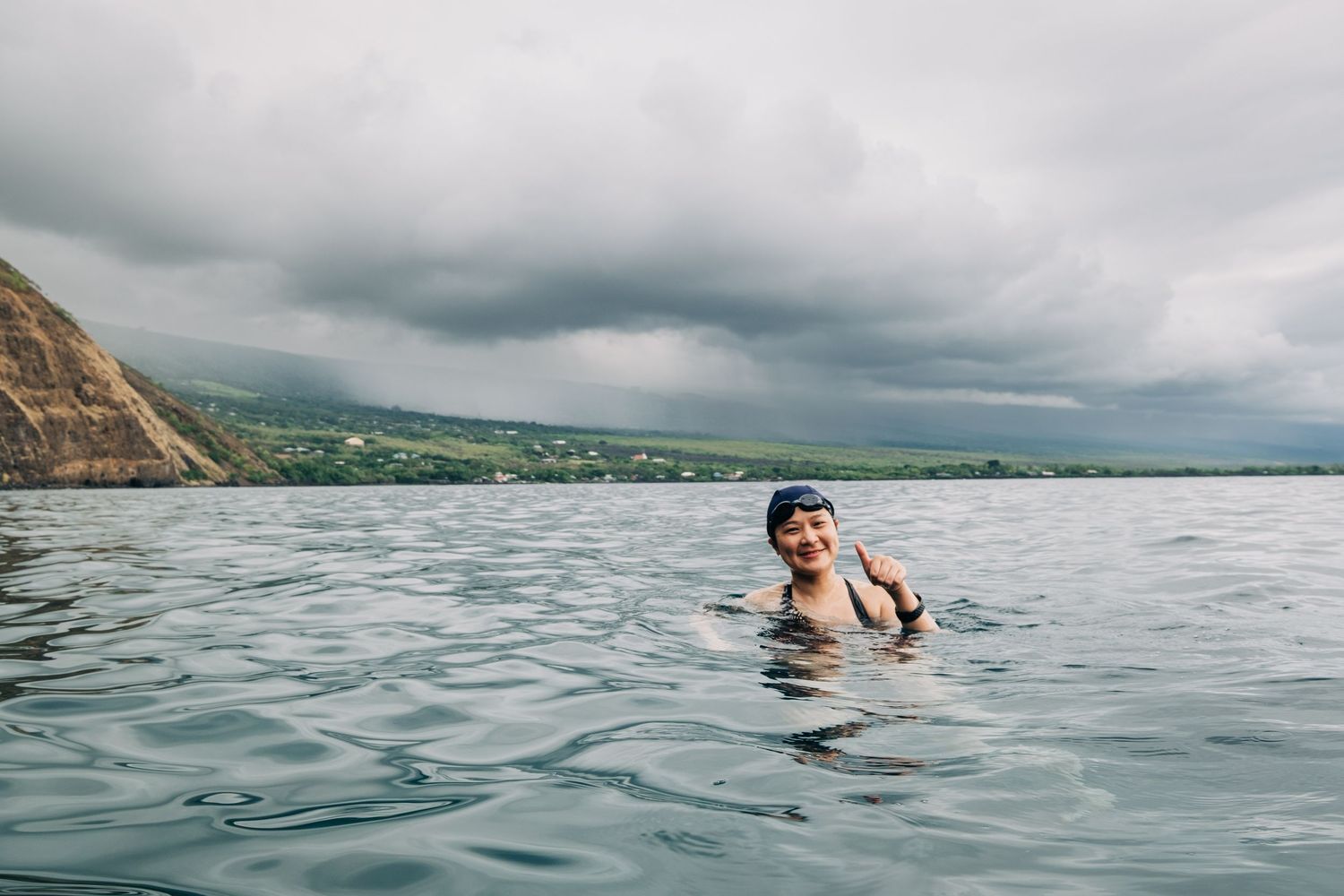 Person swimming in deep blue ocean waters near rocky Hawaiian coastline, Big Island Hawaii.