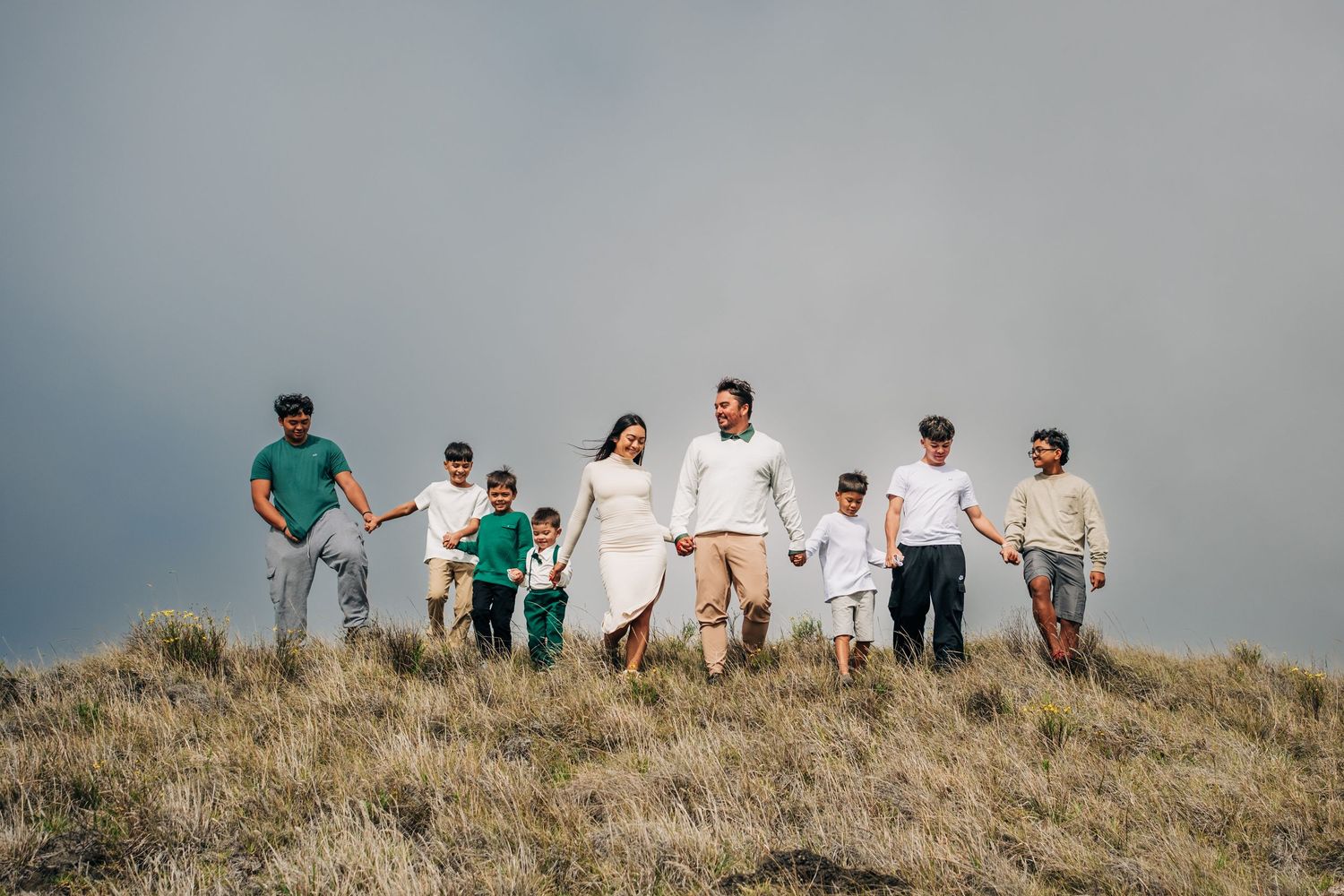 Group of people walking along grassy hilltop ridge against cloudy sky on Big Island of Hawaii.