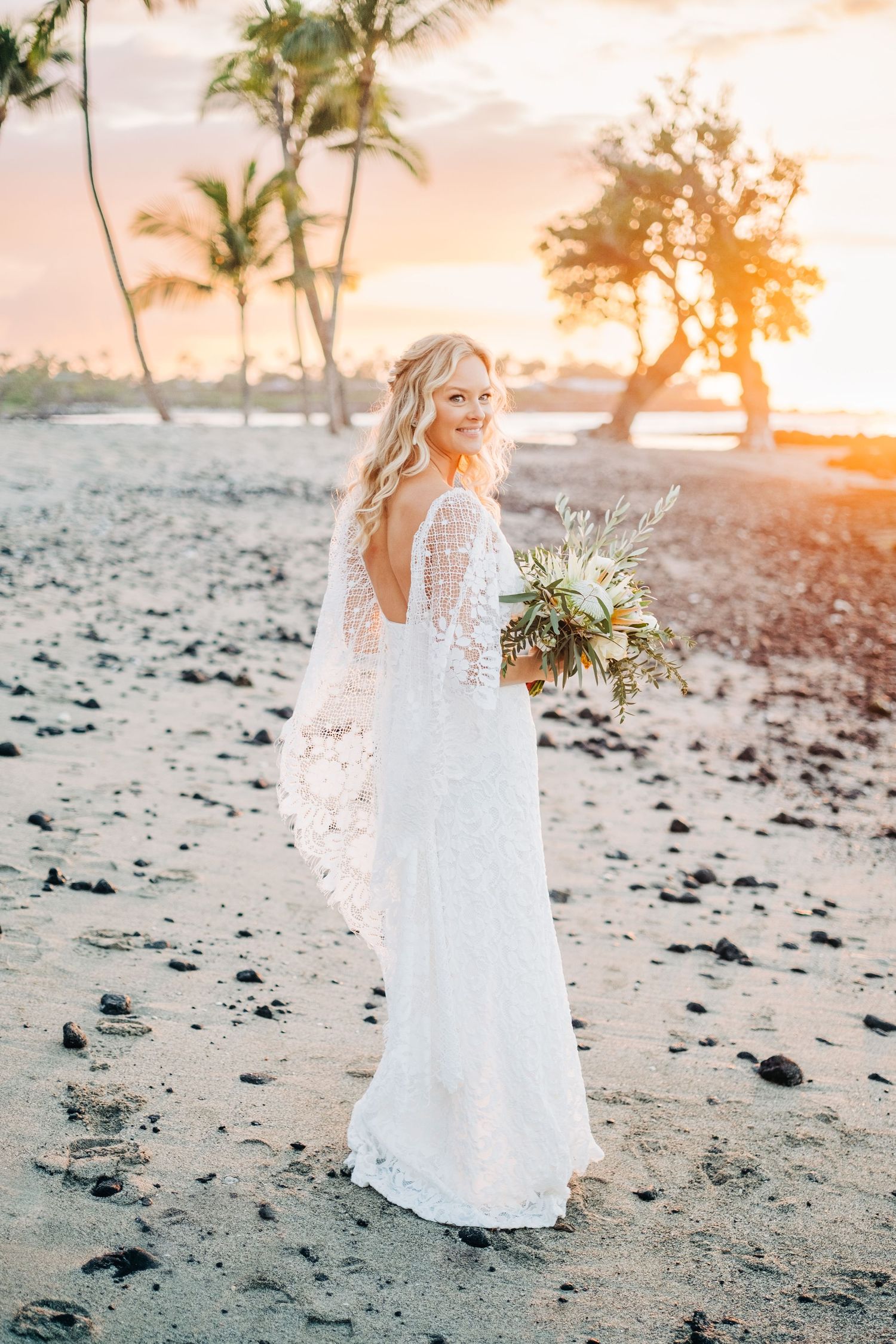 Elegant white wedding dress flowing in the breeze on a Hawaiian black sand beach at sunset at Mauna Lani Beach Resort.