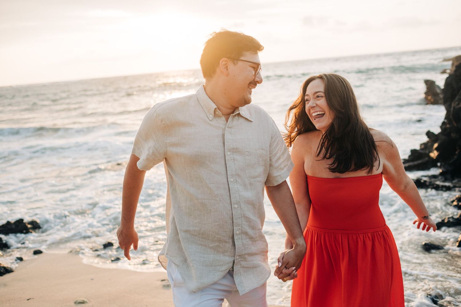 Romantic beach photoshoot with couple in red dress and white shirt against ocean backdrop on Kukio Beach, Kona, Big Island of Hawaii.