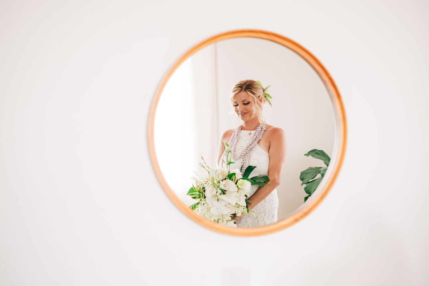 Bride with floral crown reflected in round copper mirror holding white bouquet at Kona Salt Farm, Big Island Hawaii.