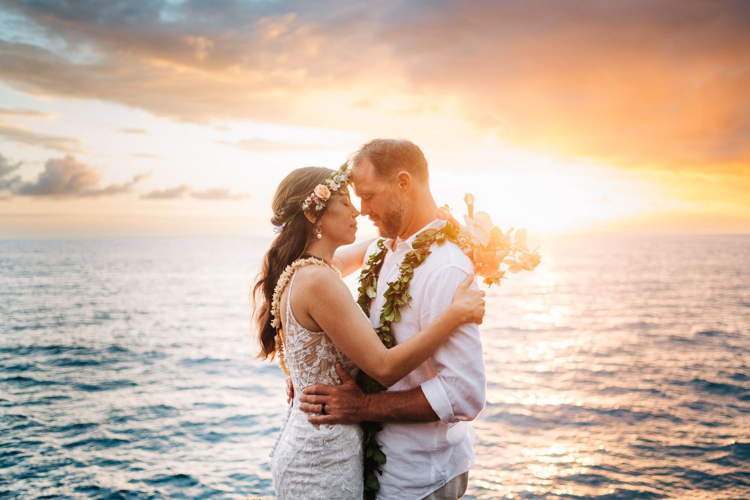 Couple shares intimate moment wearing traditional Hawaiian leis during beach sunset at Outrigger Kona Resort, Big Island Hawaii.