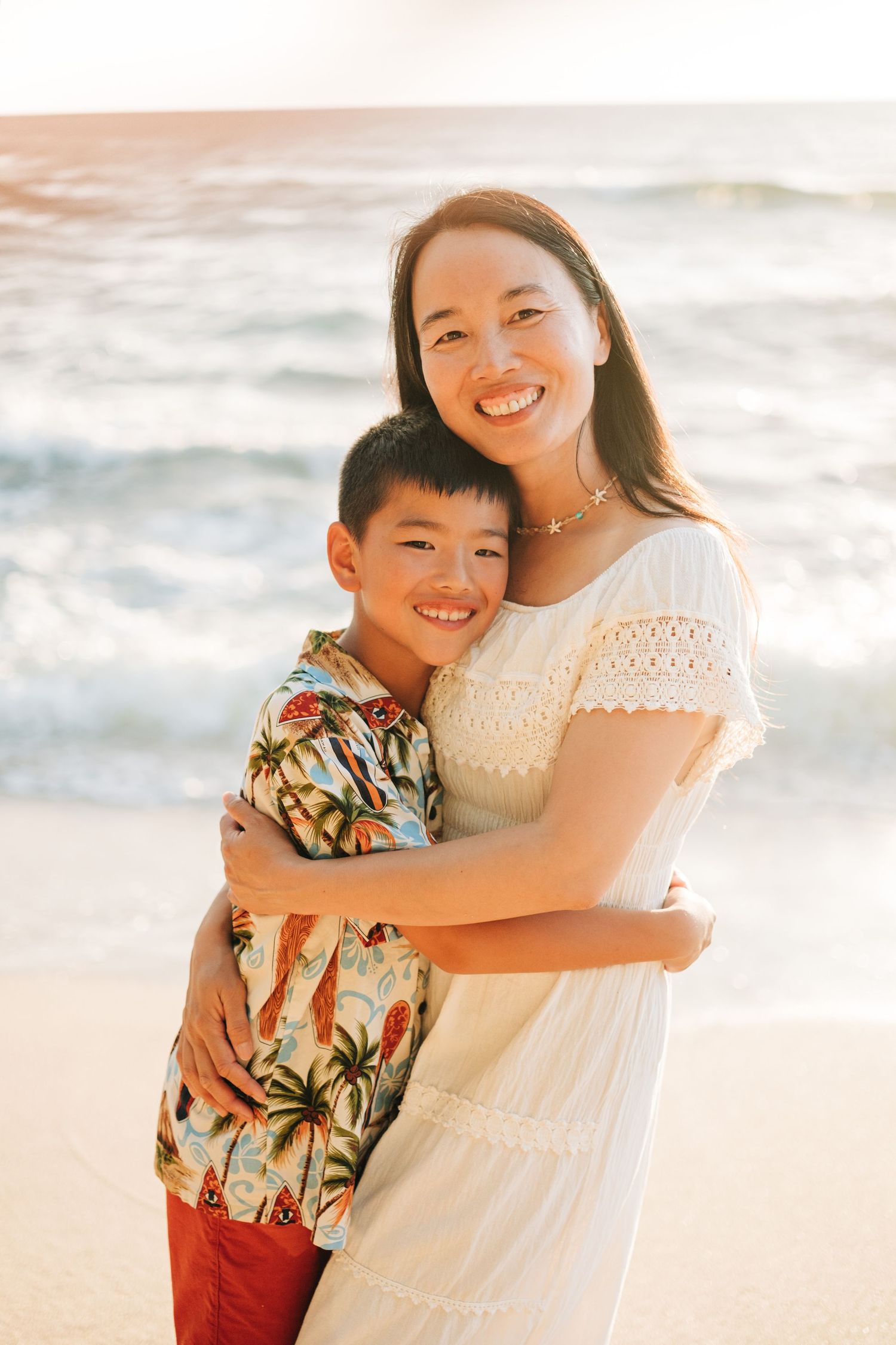 Mother and son share loving embrace on sunny beach at sunset at Kukio Beach, Kona, Big Island Hawaii.