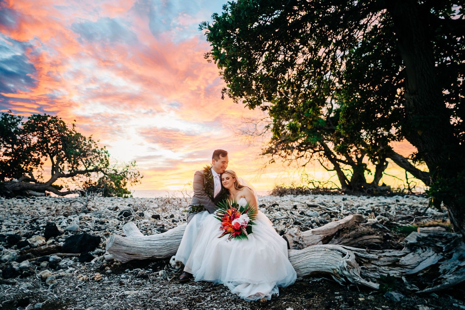 Stunning sunset wedding photos on a rocky beach with dramatic pink and orange sky at Fairmont Orchid, Big Island Hawaii.