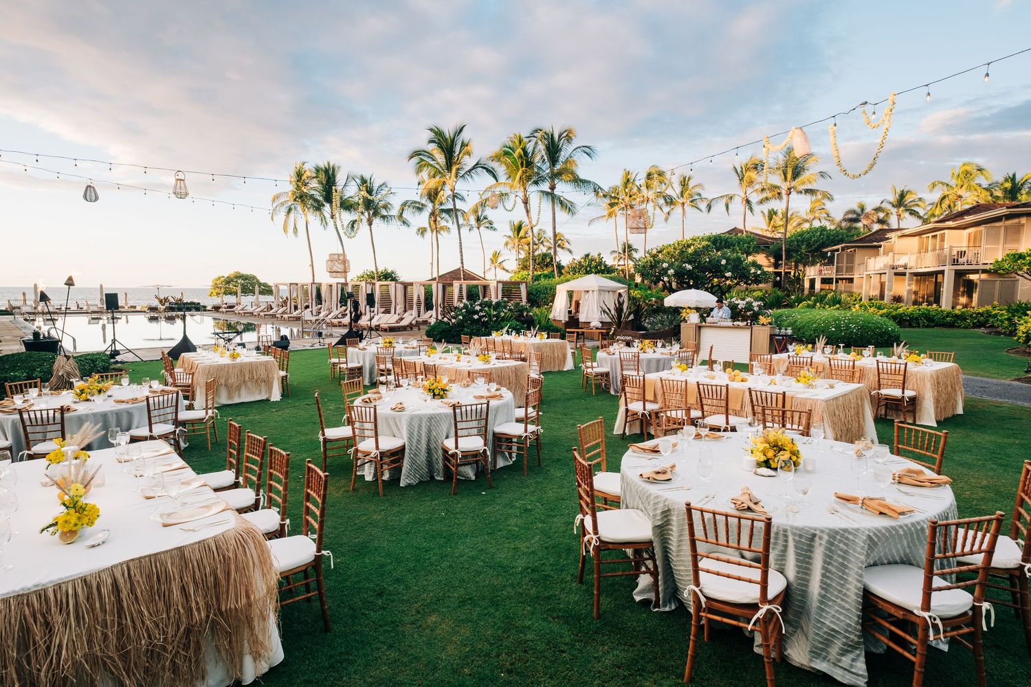 Outdoor wedding reception setup with round tables and palm trees at sunset. Four Seasons Hualalai Event.