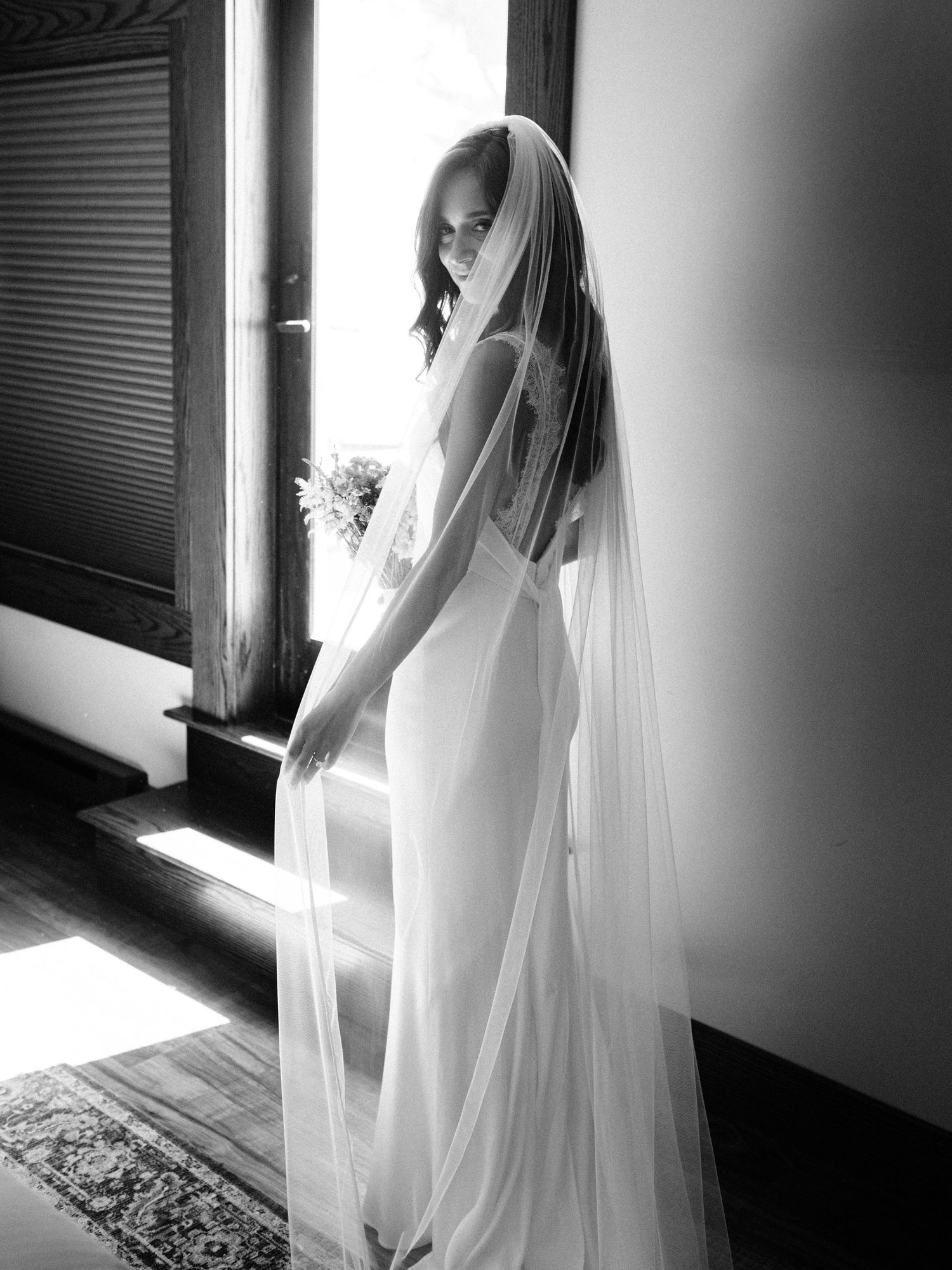 Black and white portrait of a bride in an elegant backless dress with flowing veil.