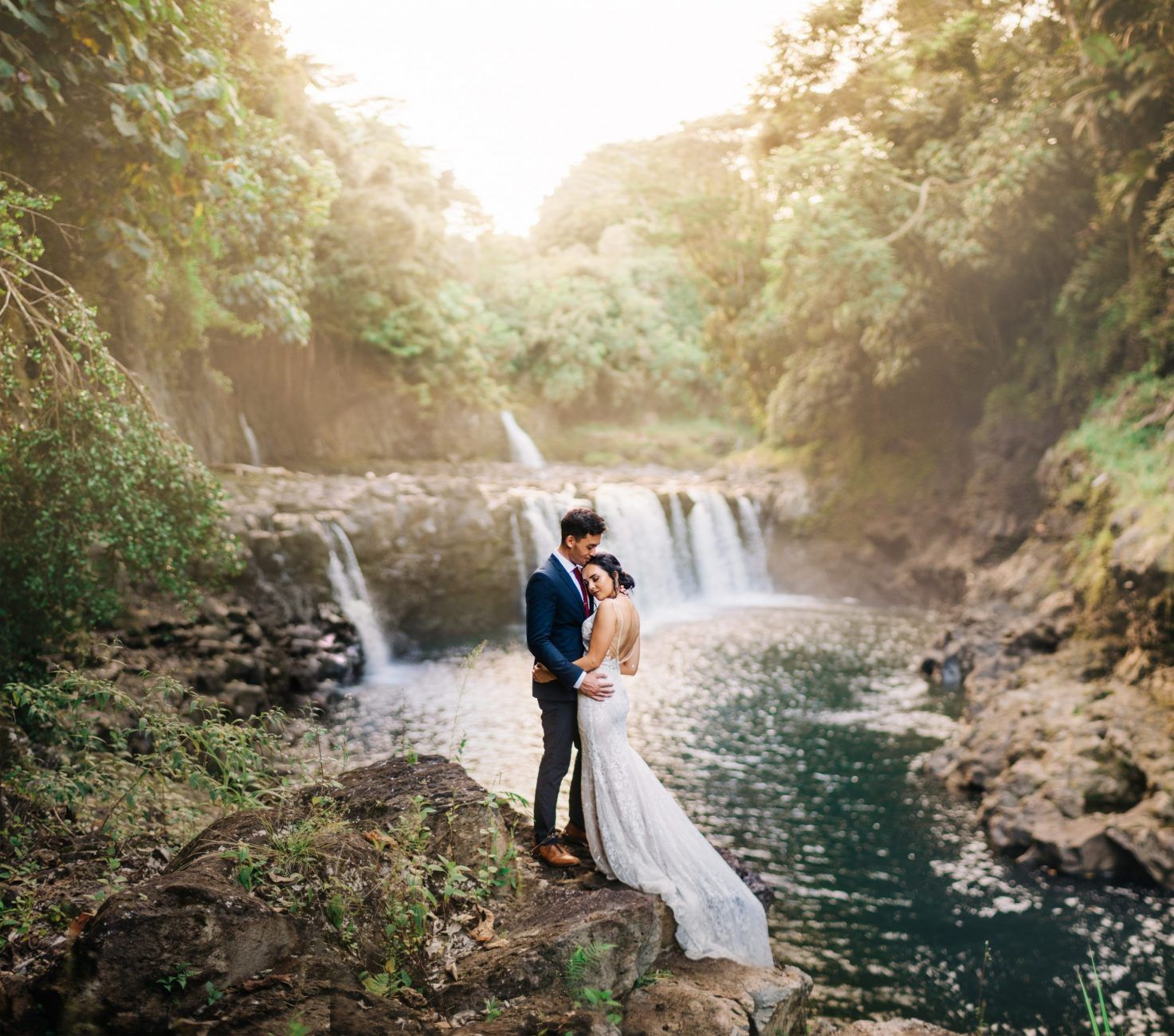 Wedding couple embracing near a scenic waterfall in a lush forest setting at the Falls at Reeds Island.