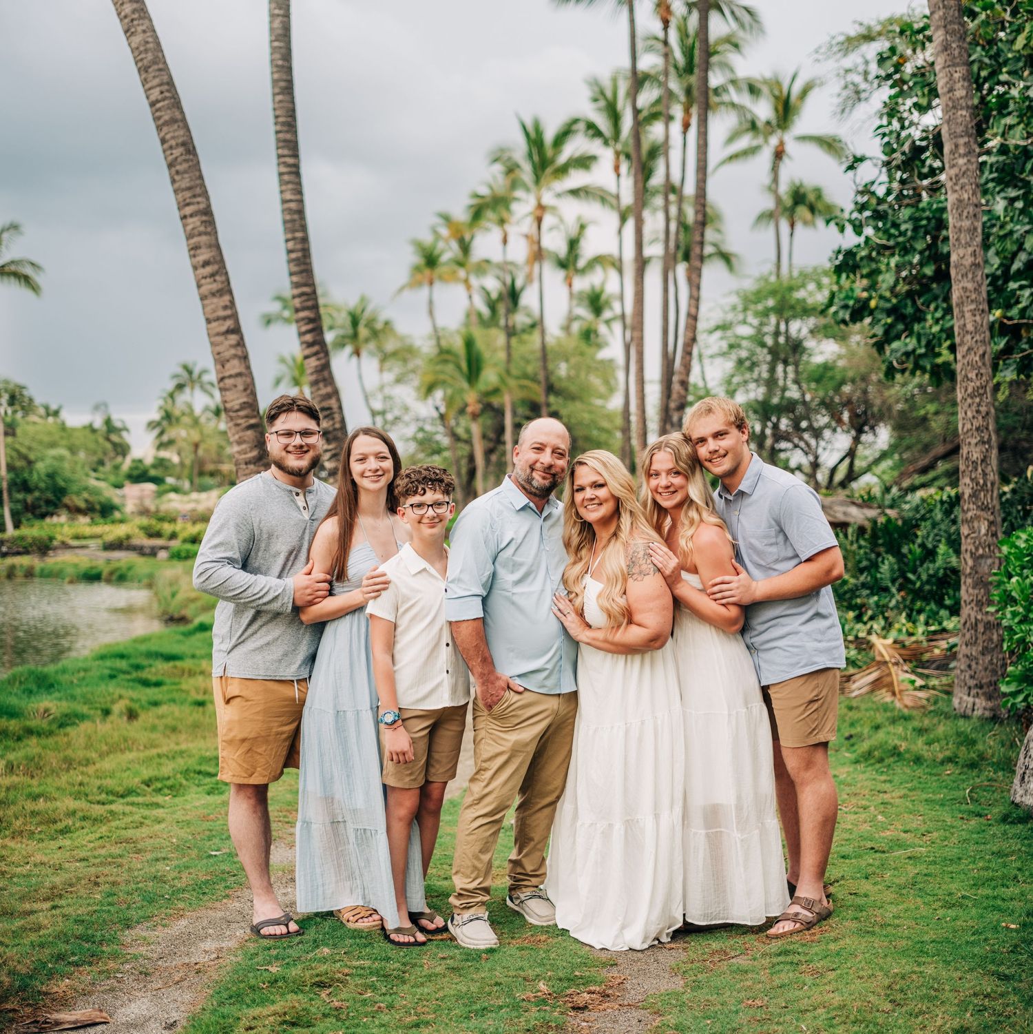 Group portrait of family members in coordinated outfits against tropical palm tree background at A-bay, Waikoloa, Big Island Hawaii.