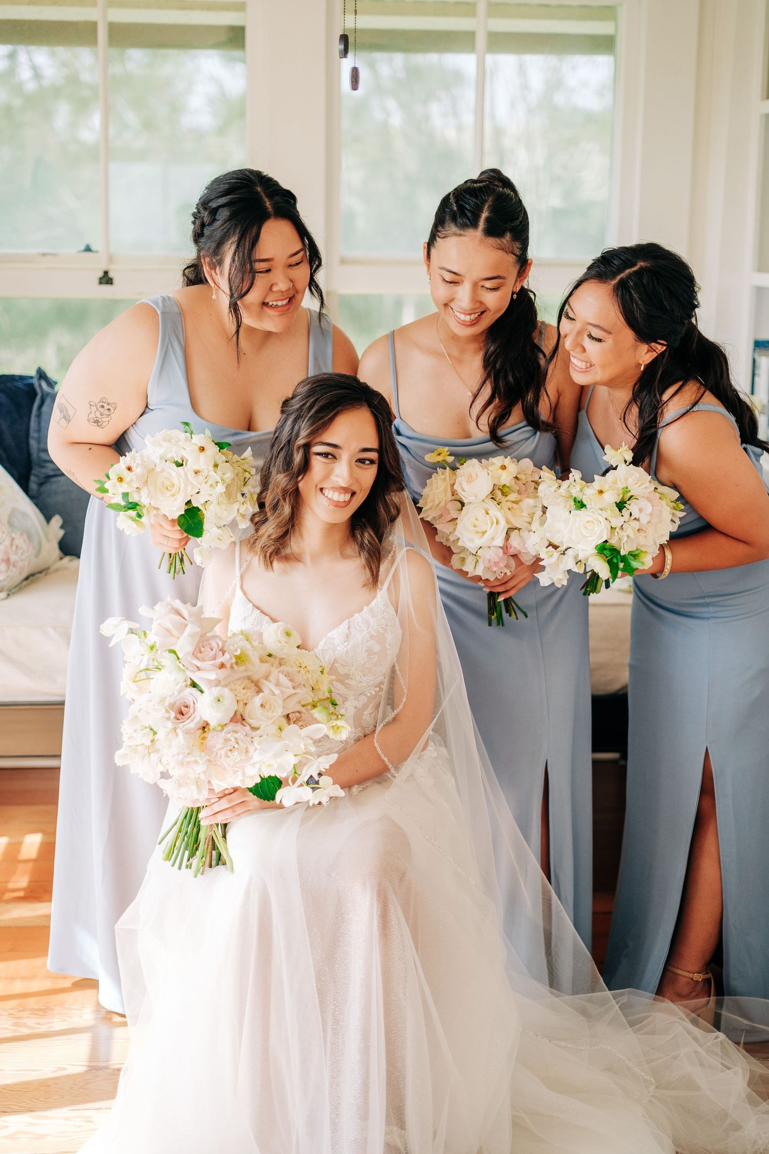 Bridal party in grey dresses poses joyfully with bouquets of pink and white flowers at Puakea Ranch, Big Island of Hawaii.