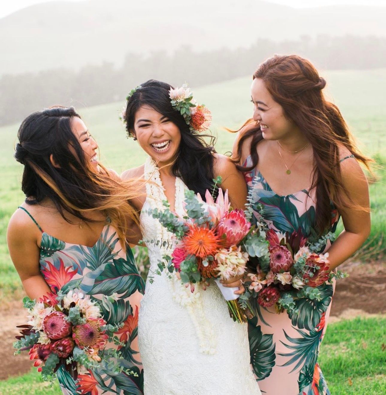 Bridesmaids in tropical print dresses holding colorful bouquets laugh together at Kahua Ranch, Big Island Hawaii.