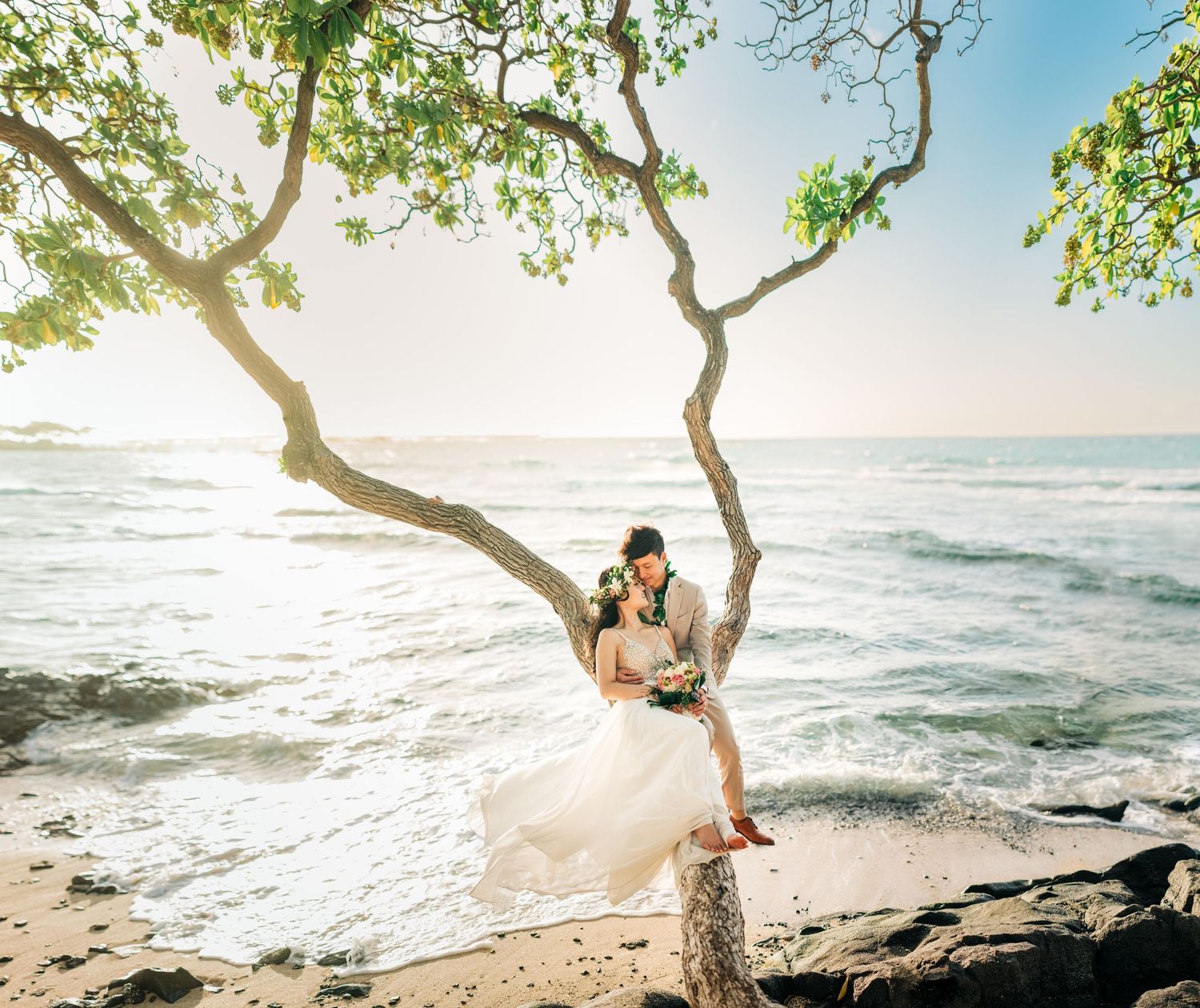 Couple shares romantic moments under a tree branch overlooking the Pacific Ocean at sunset on Kukio Beach, Big Island of Hawaii.
