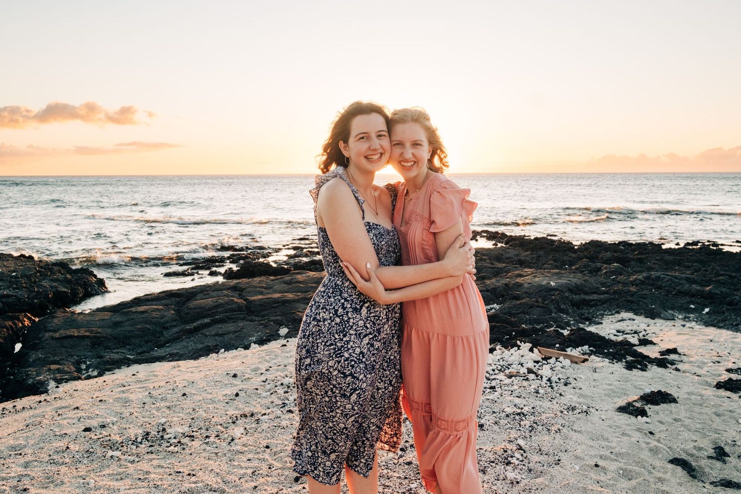 Two people embrace on rocky beach during golden sunset at Mauna Lani, Big Island of Hawaii.