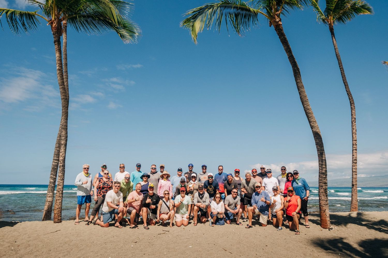 Large group gathered between palm trees on a tropical beach with ocean in the background at Mauna Lani Beach Resort.