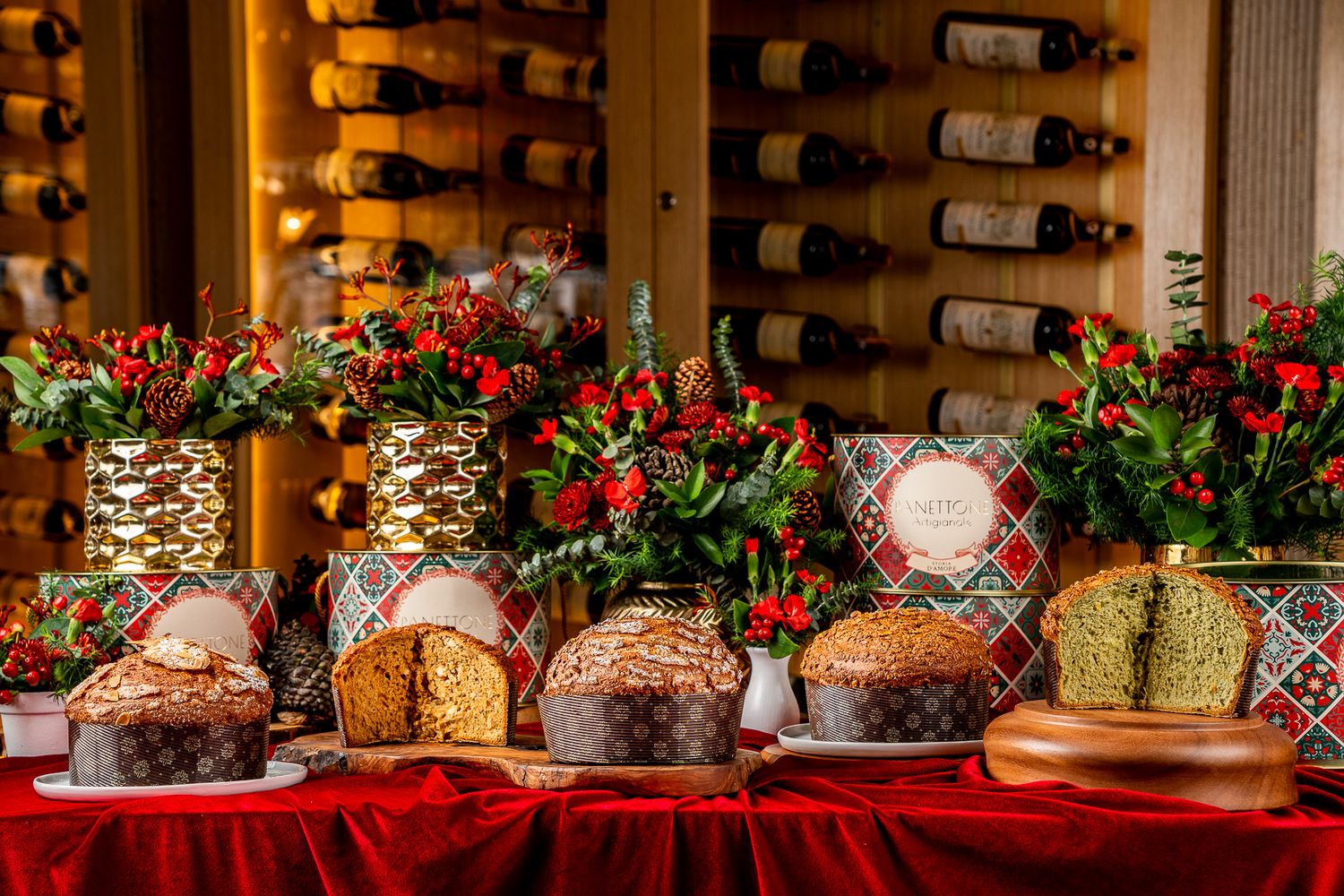 Festive holiday table display with panettone, red floral arrangements, and wine bottles in the background.