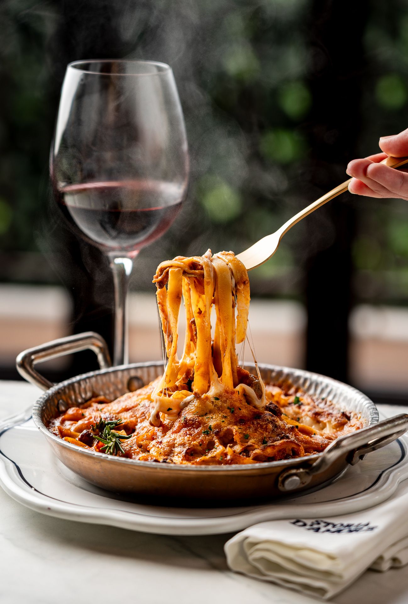 Steaming fettuccine pasta twirled on a fork in a copper pan, served with red wine at an elegant Italian restaurant.