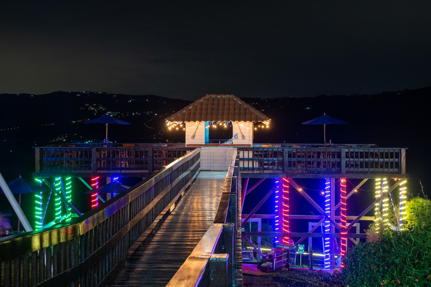 Illuminated pier with colorful neon lights leading to a gazebo at night.