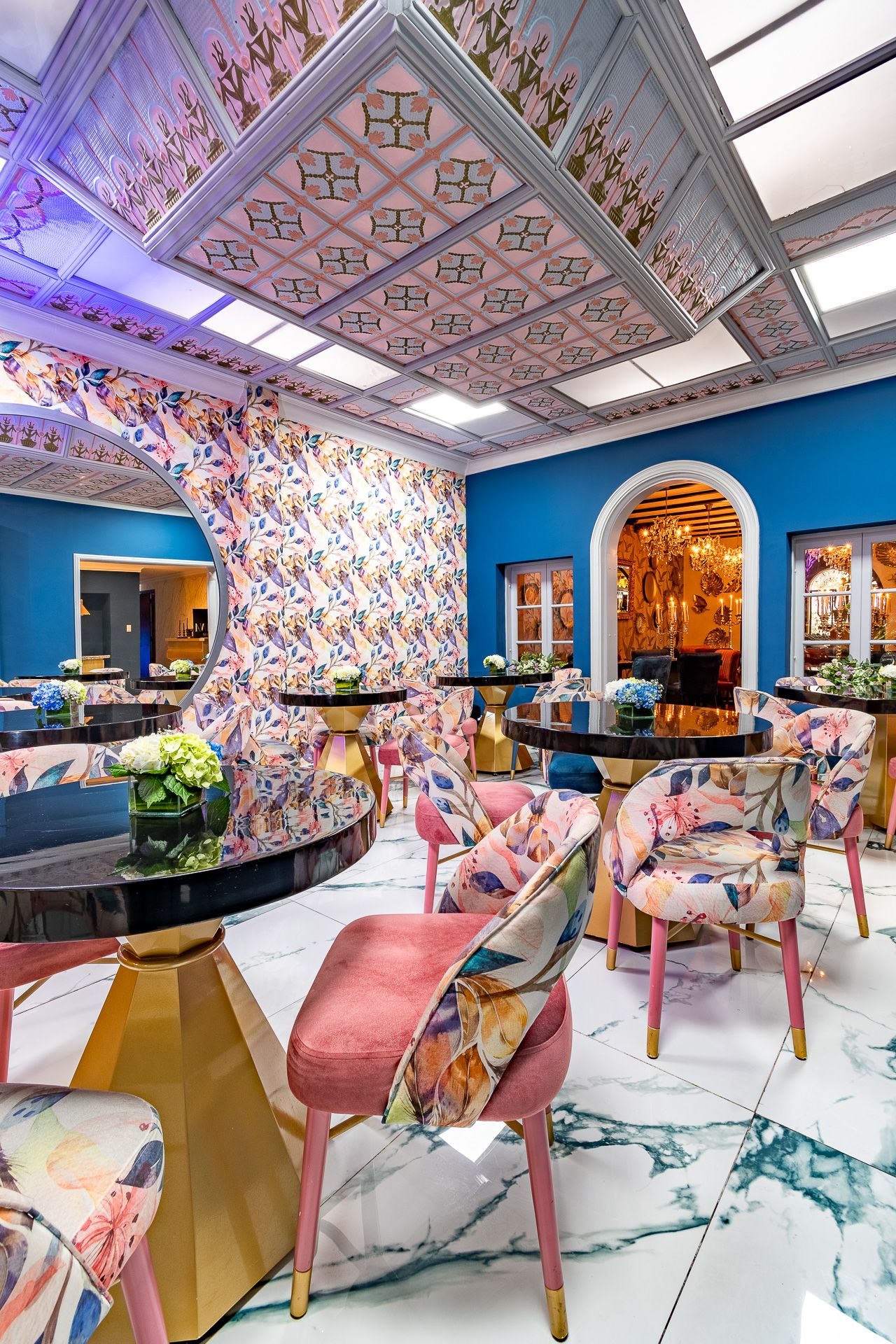 Luxurious restaurant interior with blue walls, floral chairs, marble floors, ornate ceiling, and golden accents.