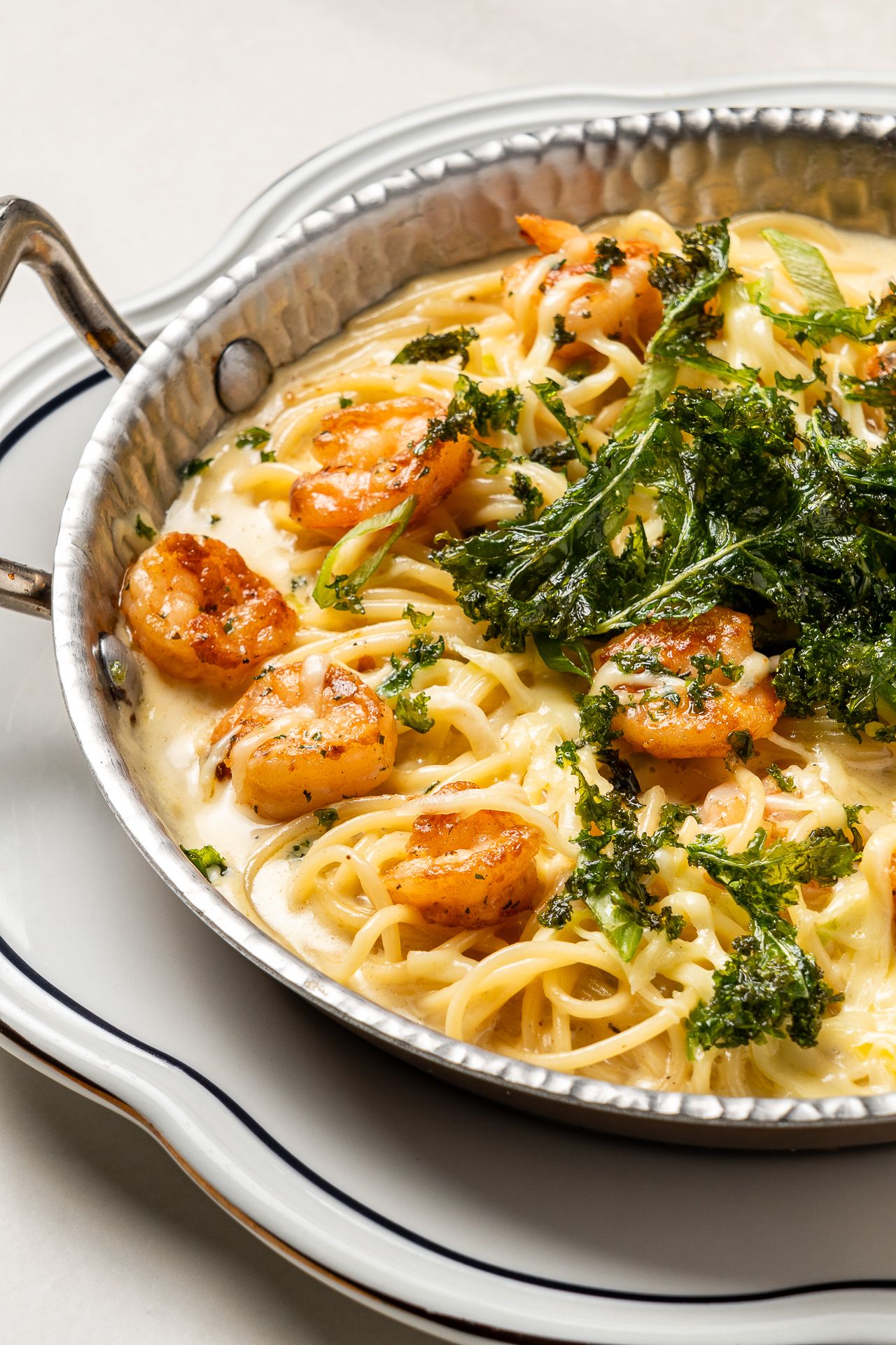 Shrimp pasta in creamy sauce topped with crispy kale, served in a silver pan on a white plate.