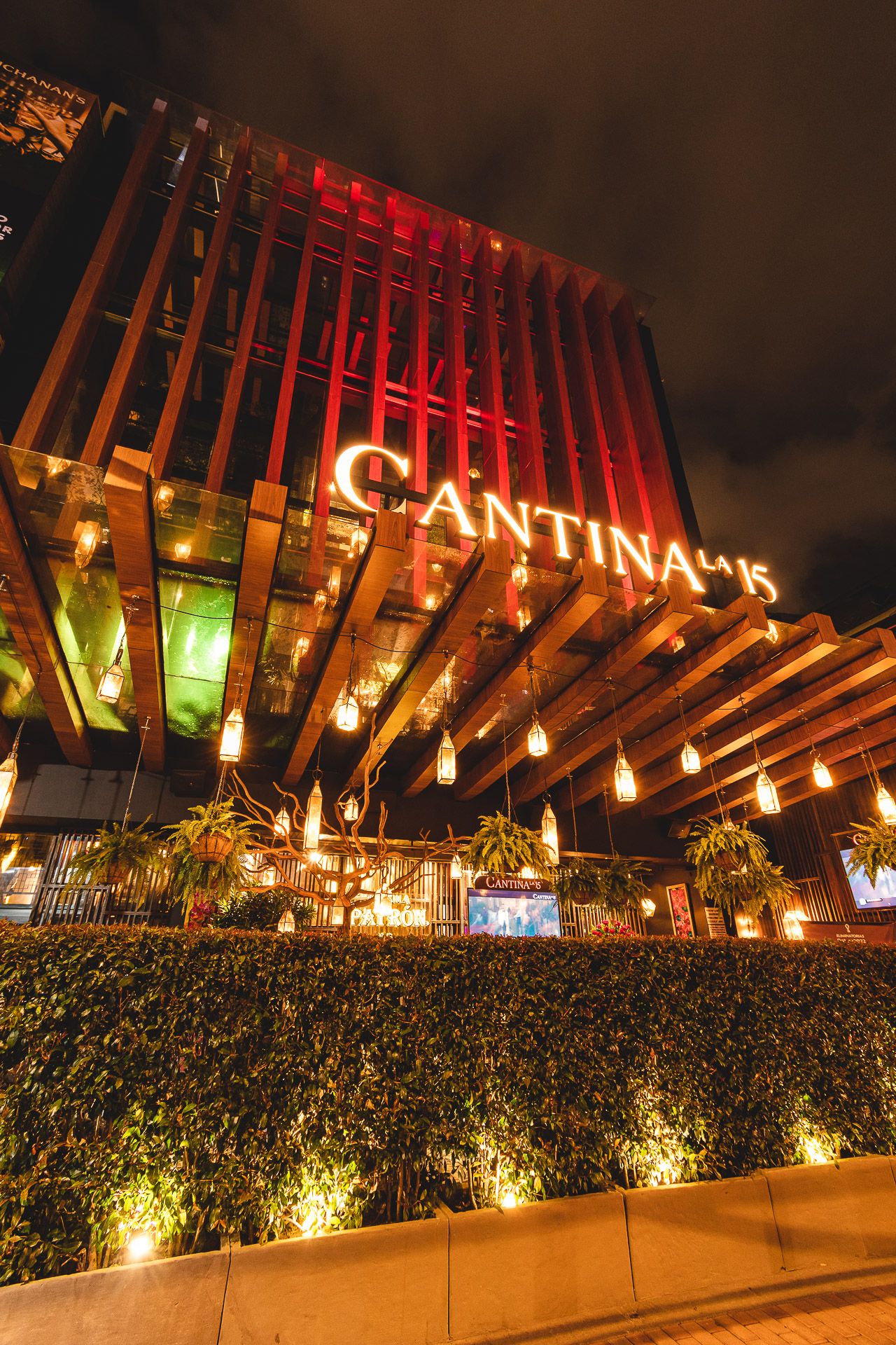 Cantina 15 restaurant exterior illuminated at night with warm Edison bulbs and red lighting against modern wooden facade.