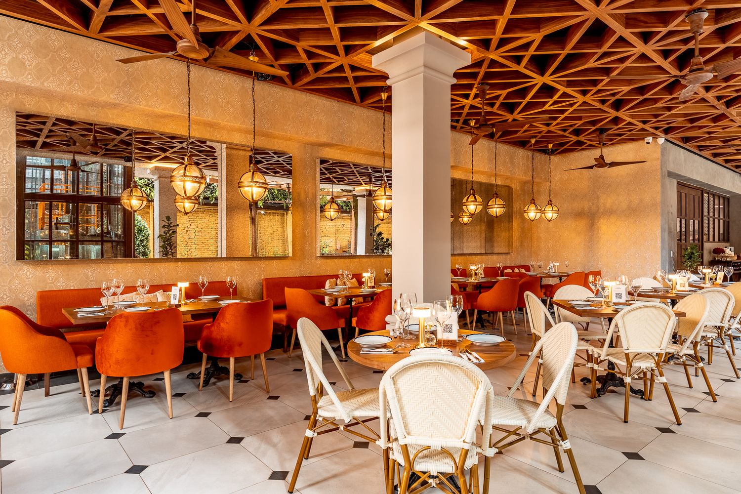Elegant restaurant interior with orange velvet chairs, white bistro seats, wooden lattice ceiling, and warm ambient lighting.