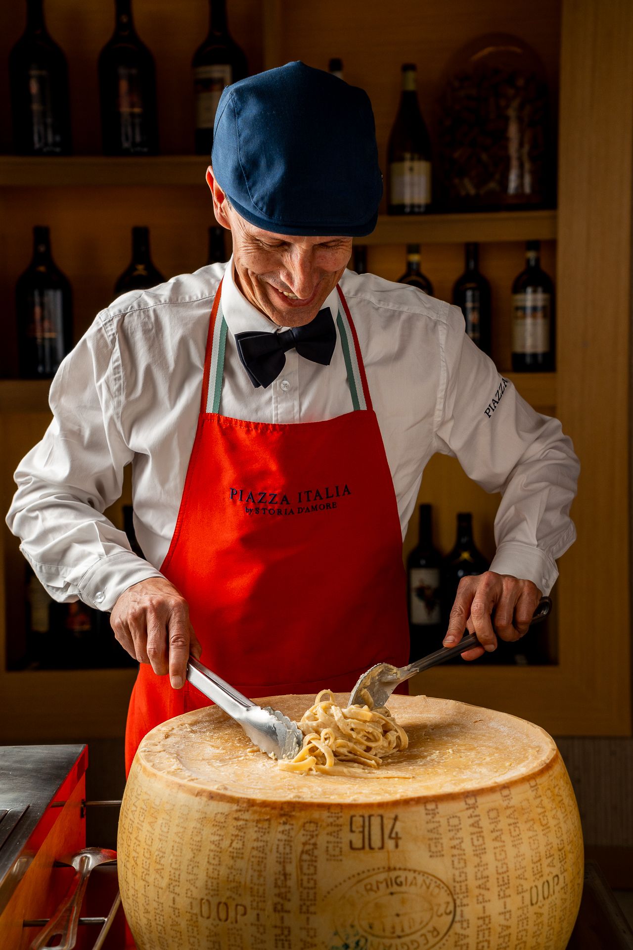 Chef serving fresh pasta from a whole Parmigiano Reggiano wheel at an Italian restaurant.