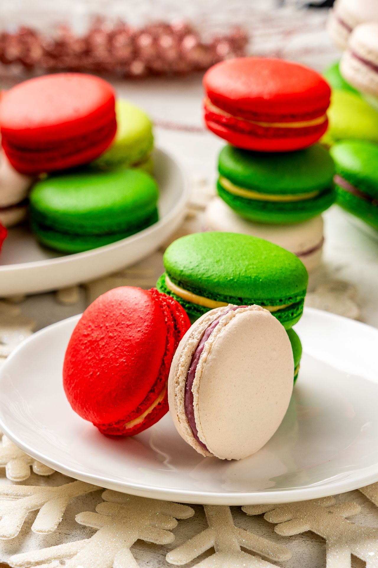 Colorful red, green, and white French macarons stacked on white plates with a festive Christmas holiday theme.