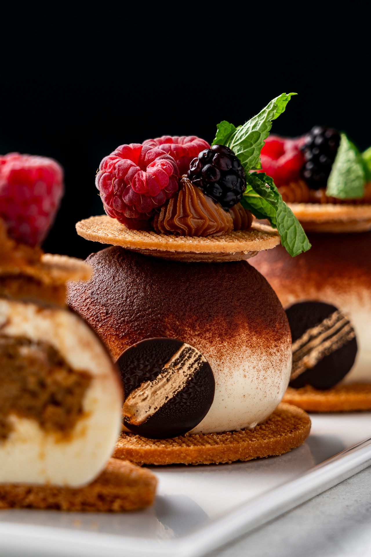 Elegant chocolate tiramisu dessert topped with fresh raspberries, blackberries, and mint leaves on a white plate.