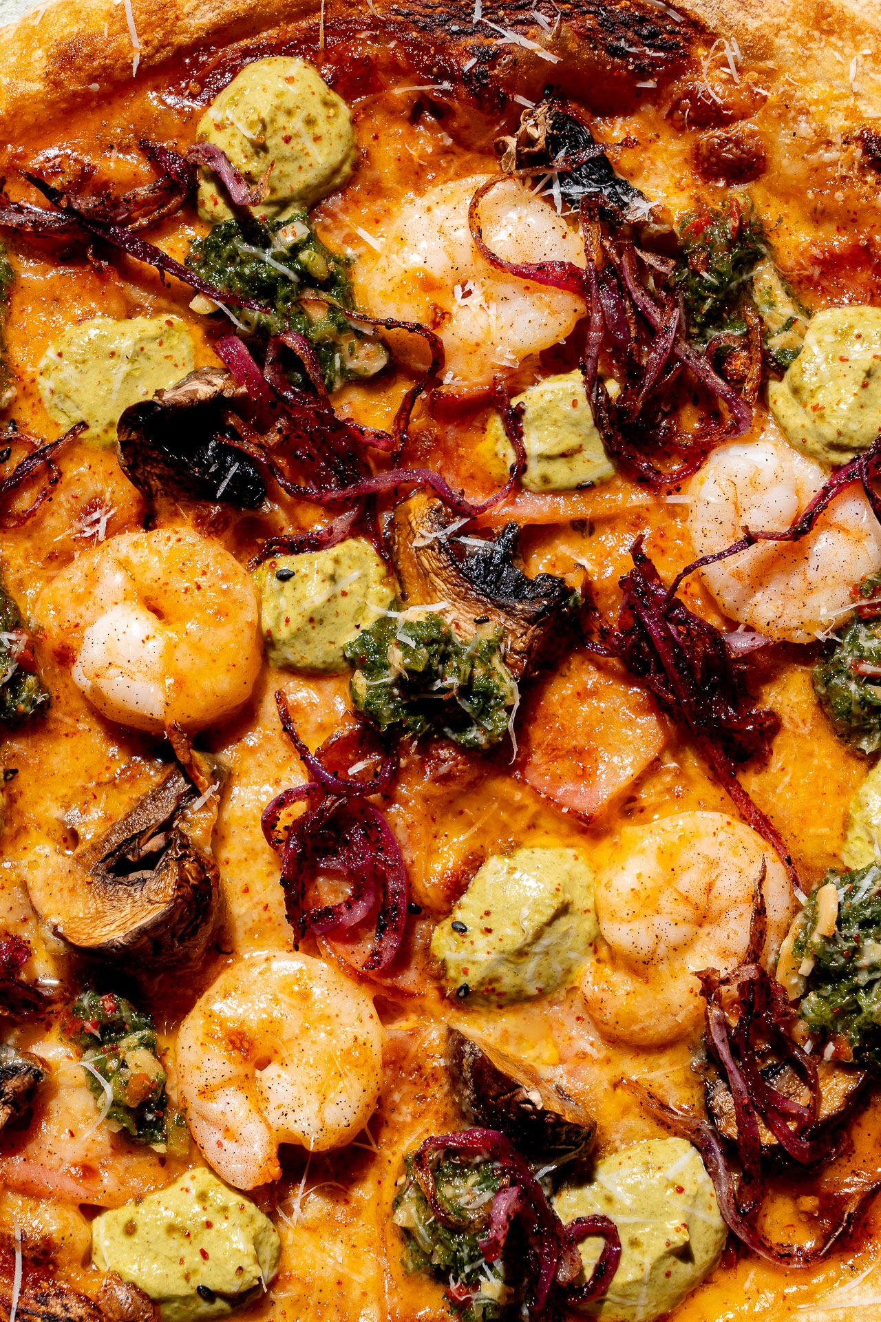 Close-up of a gourmet shrimp pizza topped with pesto, caramelized onions, mushrooms, and melted cheese.