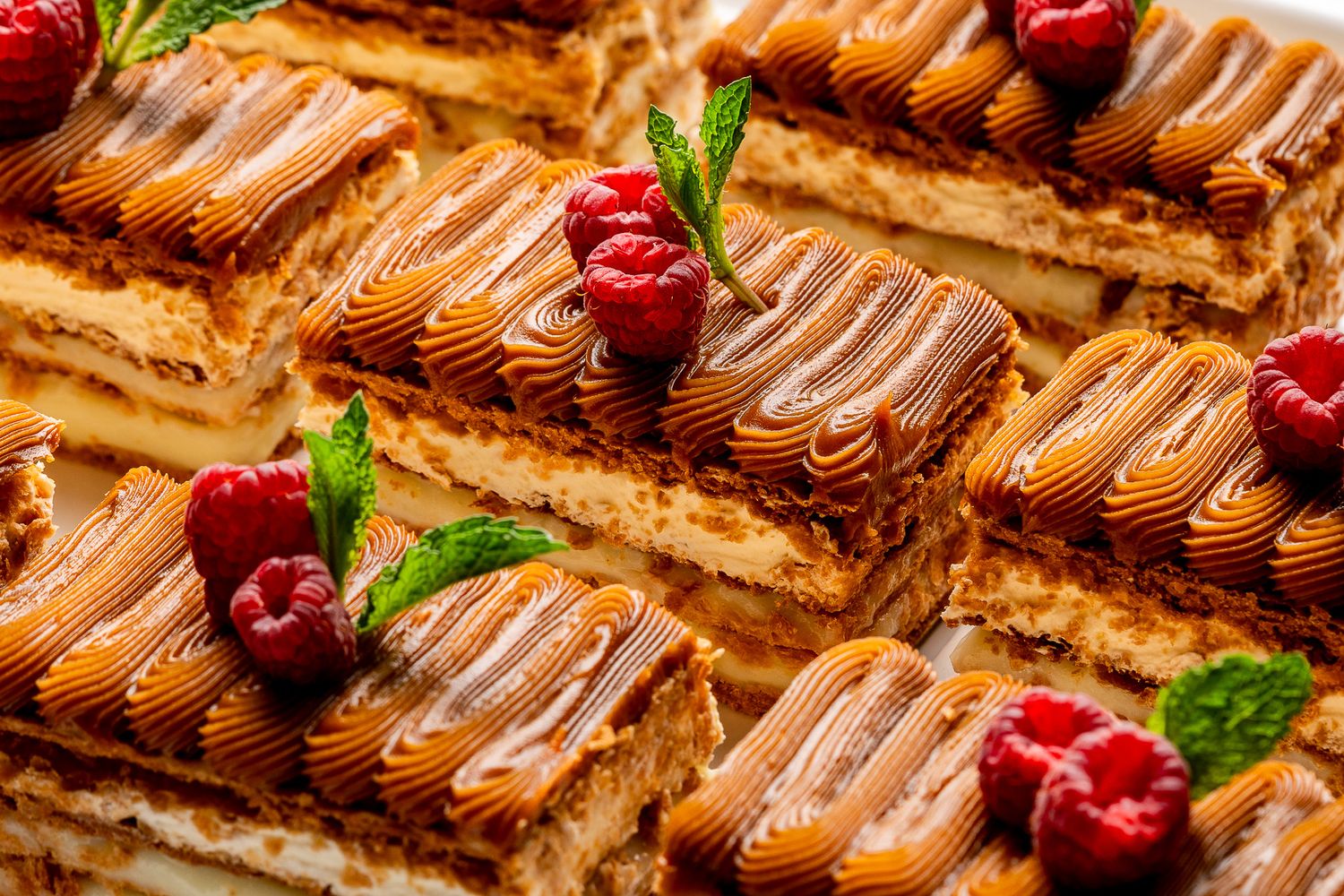 Close-up of elegant layered caramel cake slices topped with swirled frosting, fresh raspberries, and mint leaves.