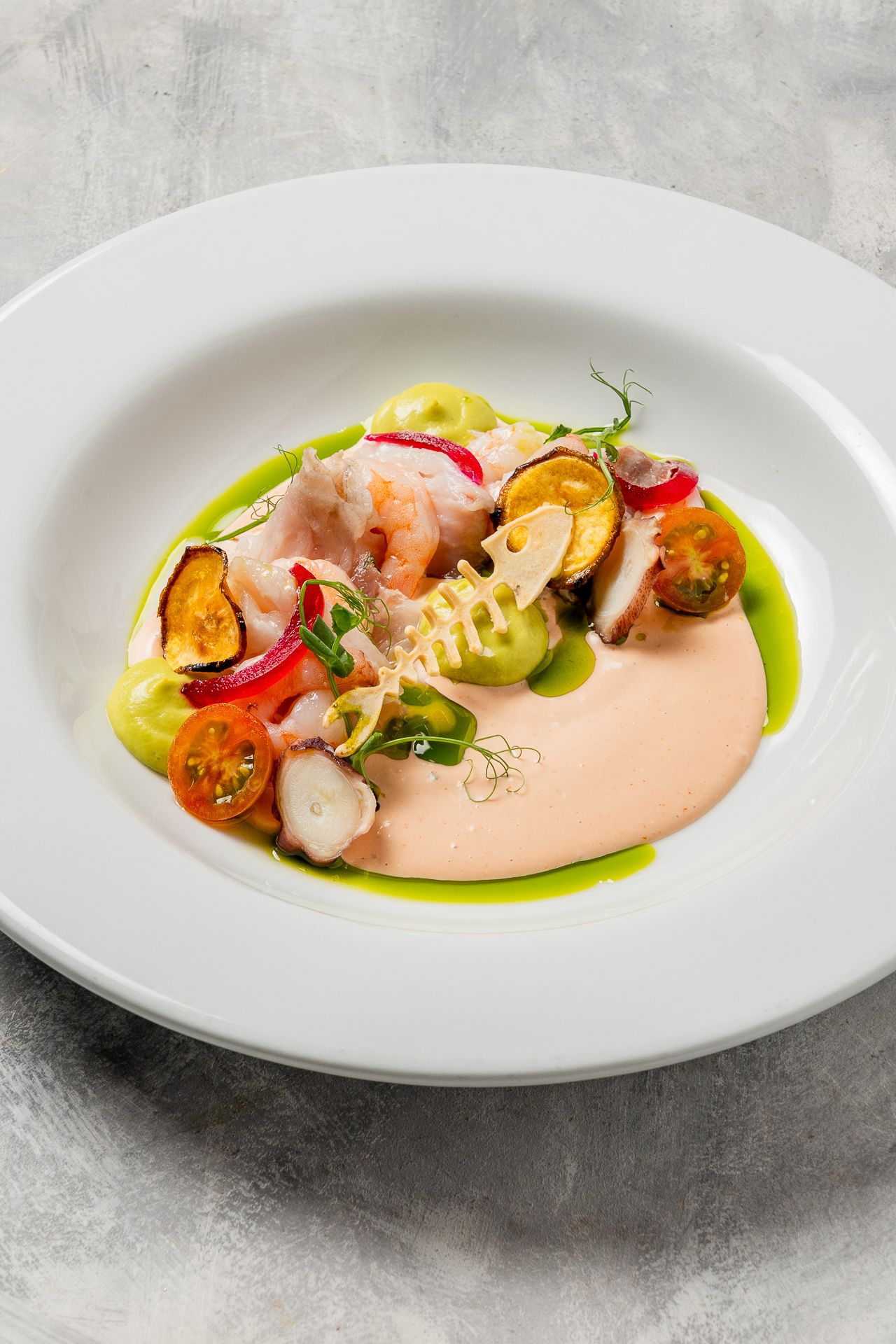 Elegant seafood ceviche with shrimp, cherry tomatoes, zucchini, and creamy pink sauce on a white plate.