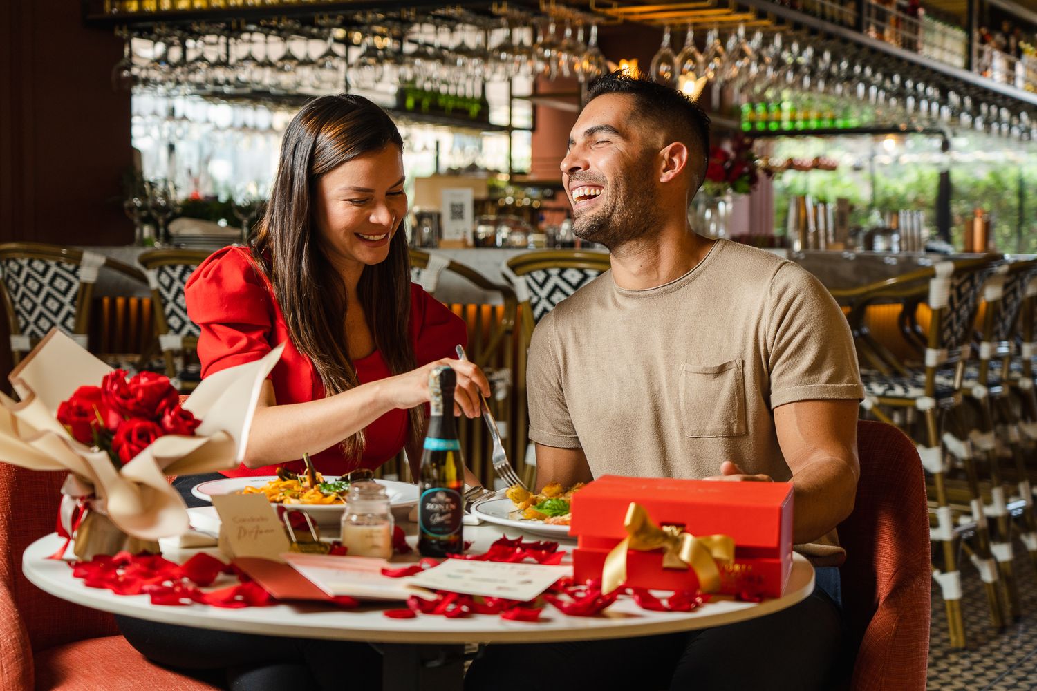 Couple enjoying a romantic Valentine's Day dinner date at a restaurant with roses, gifts, and champagne on the table.