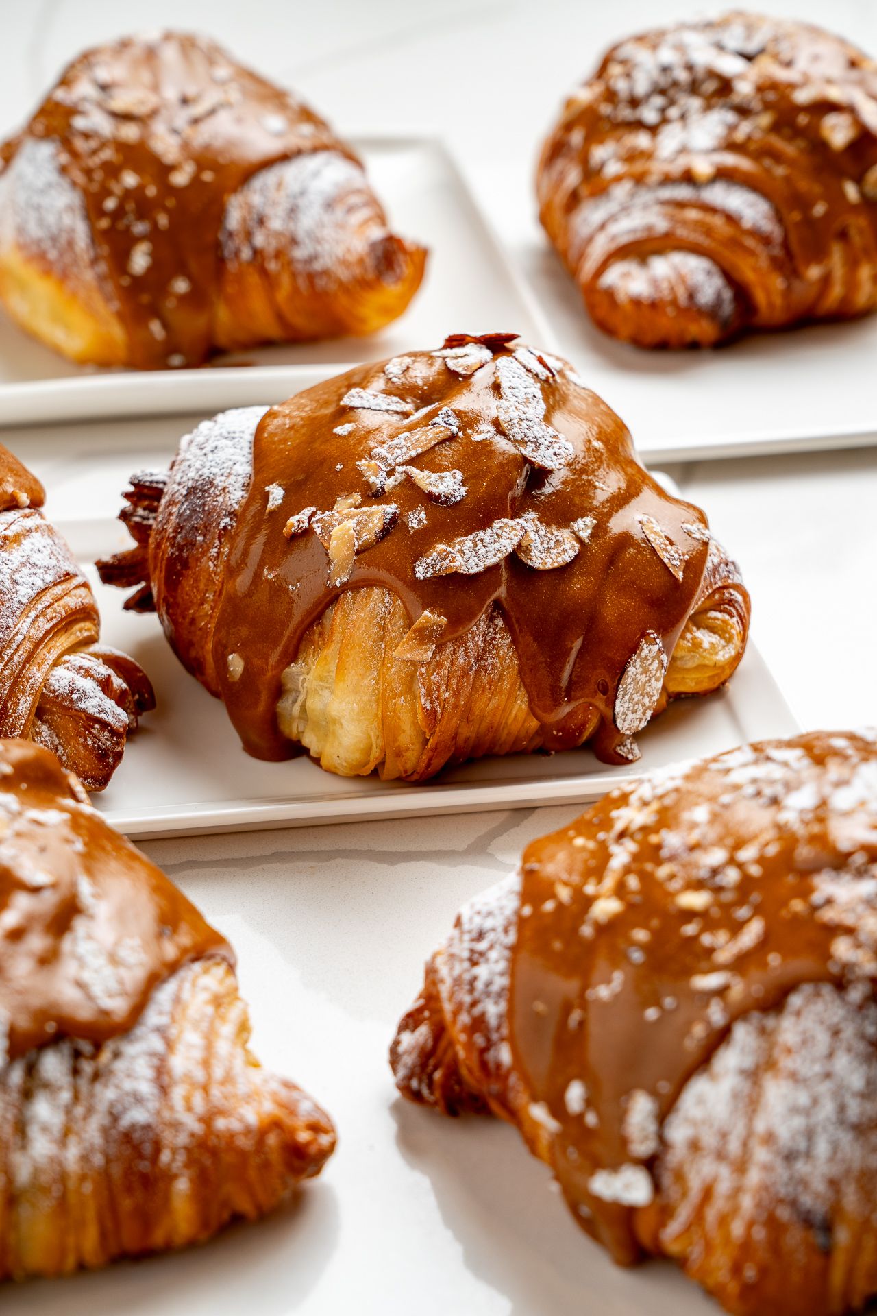 Freshly baked croissants topped with sliced almonds and powdered sugar on white plates.