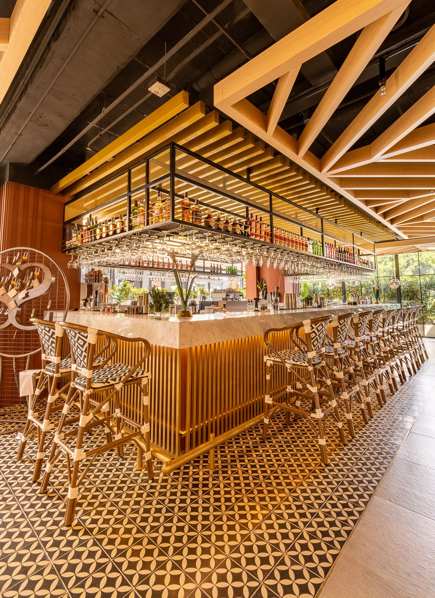 Elegant restaurant bar with gold stools, geometric tile floors, hanging glasses, and warm wood ceiling accents.