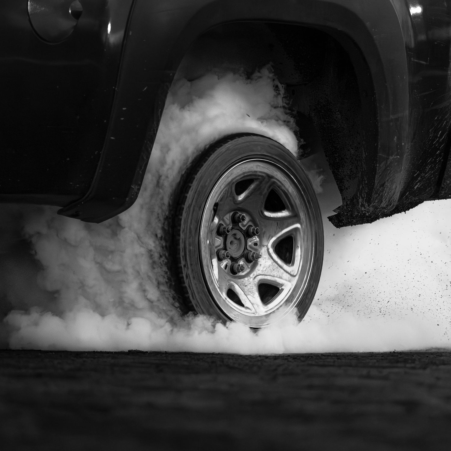 Black and white close-up of a truck wheel spinning during a burnout, producing heavy clouds of tire smoke.