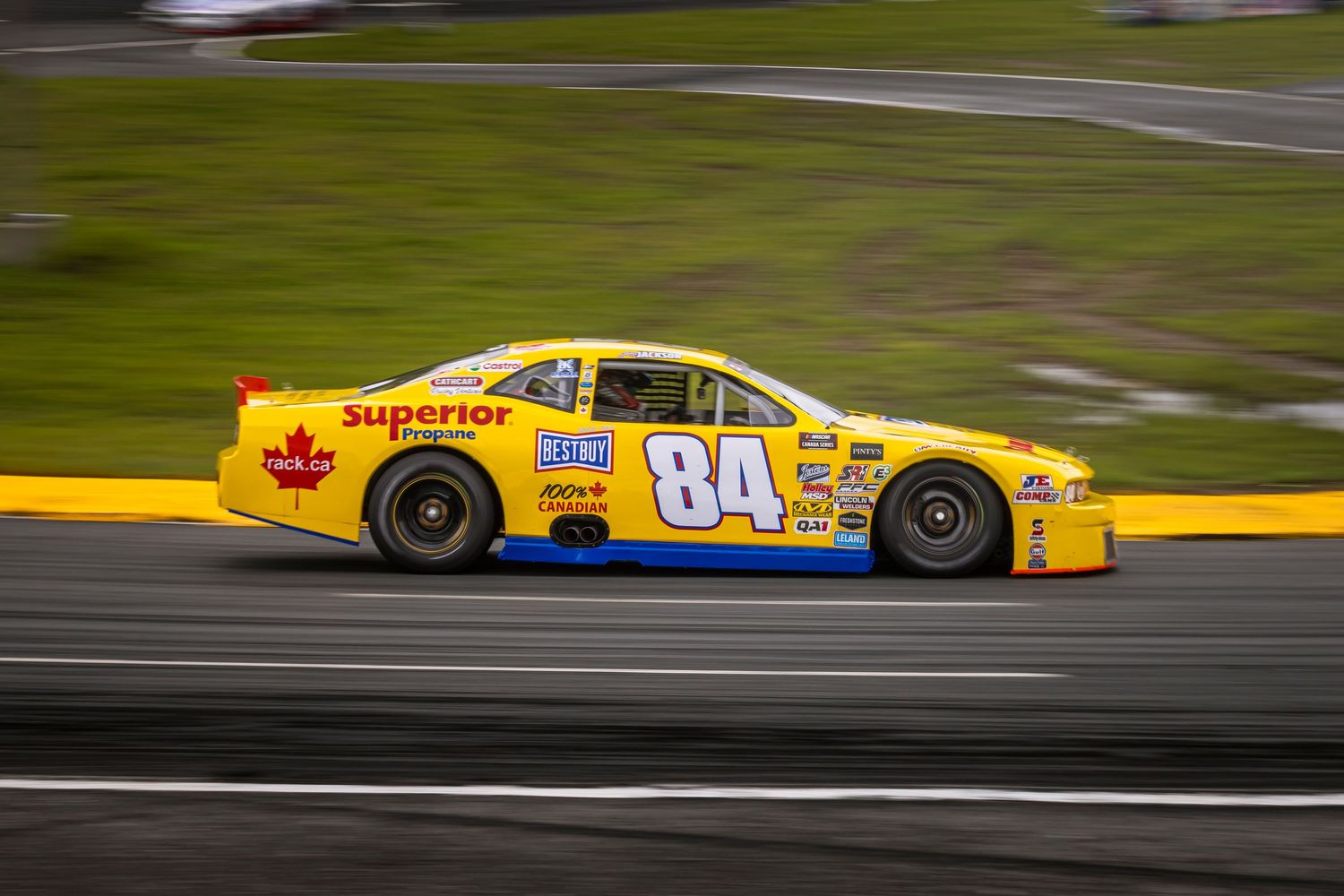 Yellow number 84 stock car speeding along the track in a motion-blurred side view.