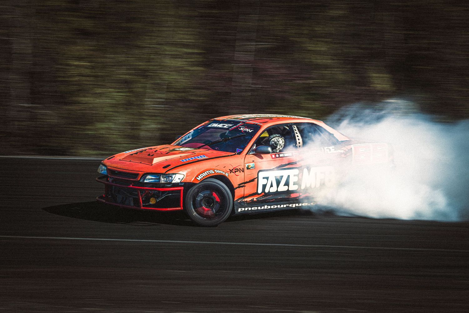 Orange Fazemag drift car sliding through a corner on a racetrack with white tire smoke trailing behind.