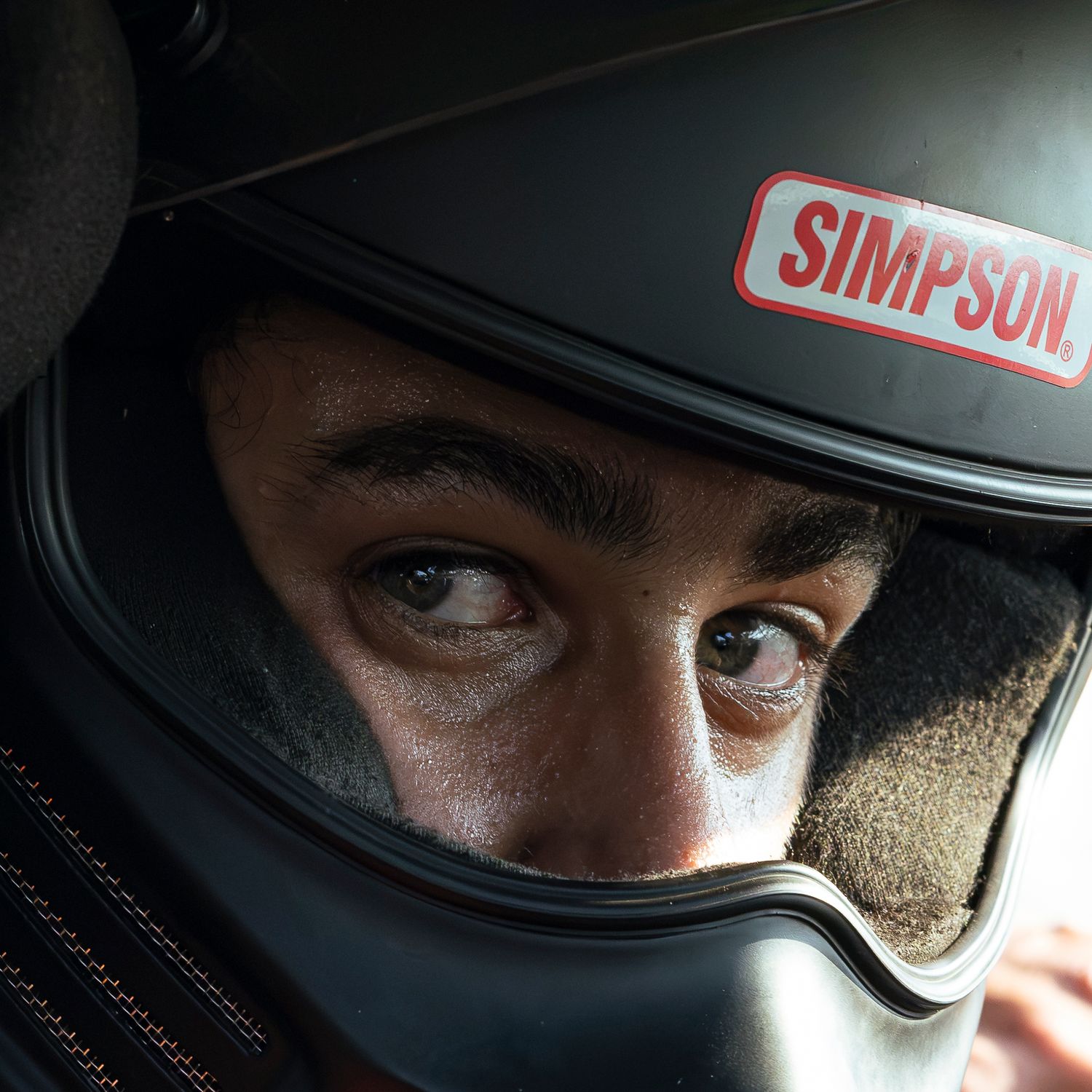 Close-up of a race driver's eyes inside a black Simpson racing helmet, looking intently to the side.