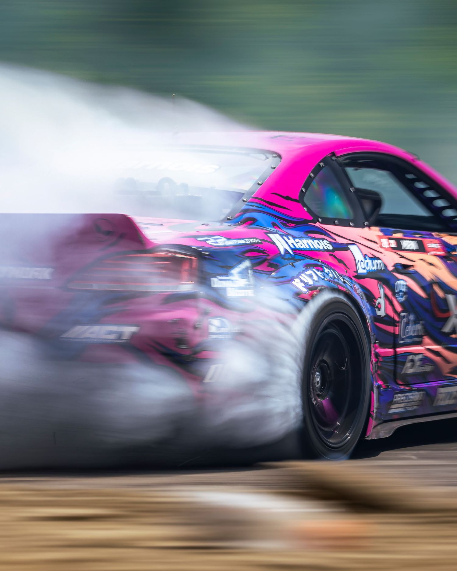 Pink and blue livery drift car sliding sideways through a corner while billowing thick tire smoke on a track.