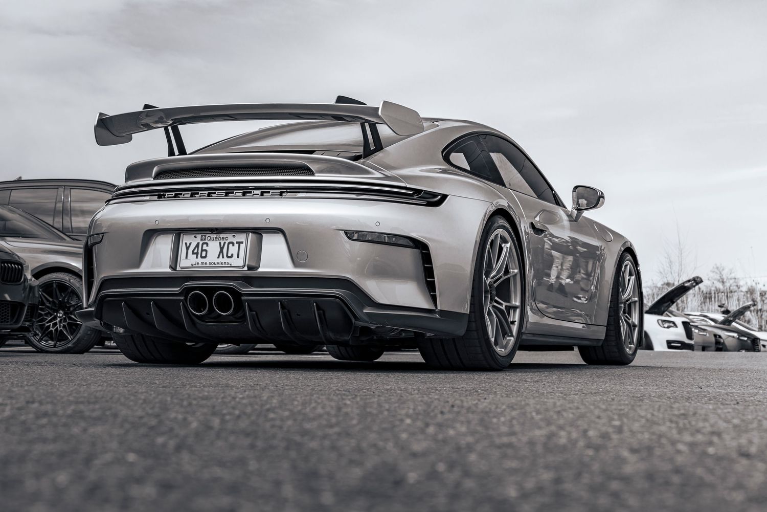 Rear three-quarter view of a silver Porsche 911 GT3 with a large fixed rear wing and quad exhaust tips parked at an outdoor car show.