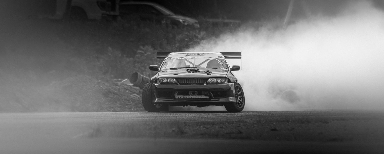 Black and white photo of a drift car sliding sideways through a thick cloud of tire smoke.
